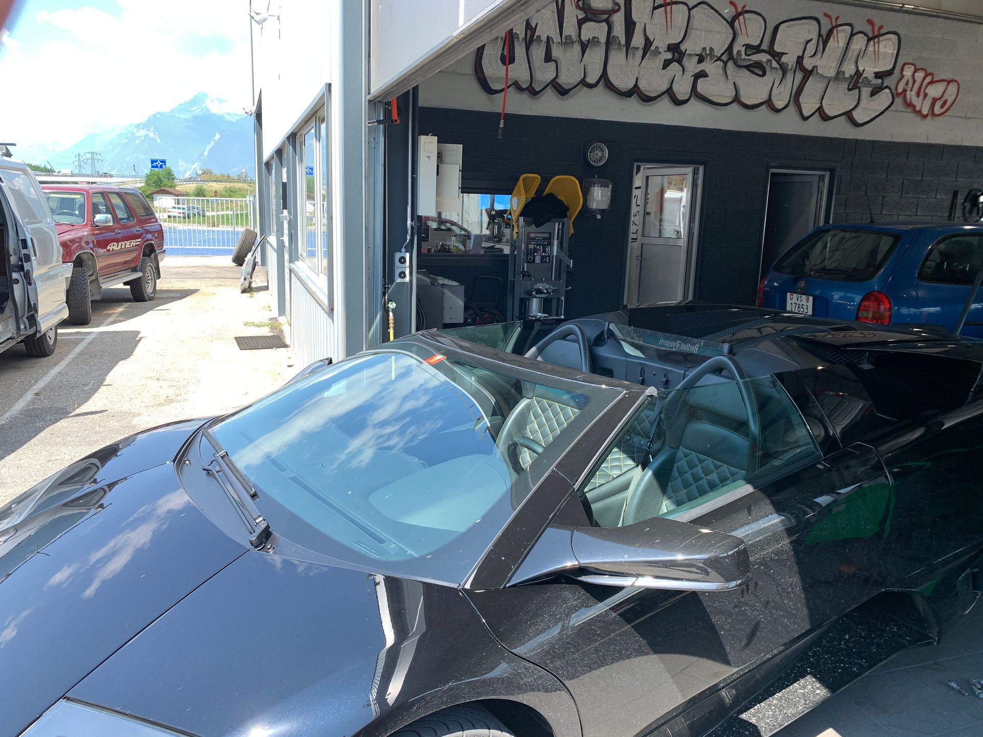 Une voiture noire est garée devant un immeuble avec des graffitis dessus.