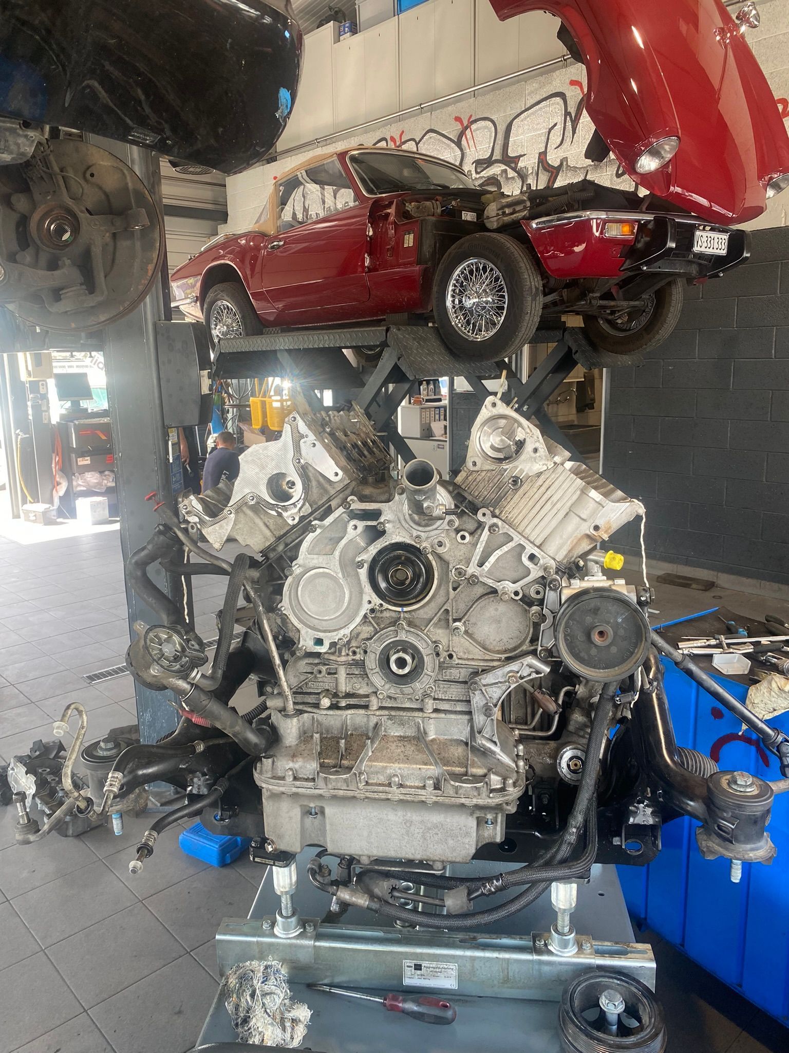 Une voiture rouge est posée sur un moteur dans un garage.