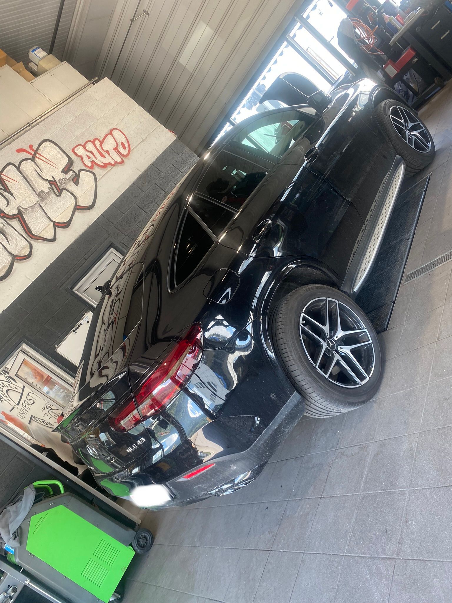 Une voiture noire est garée dans un garage avec des graffitis sur le mur.