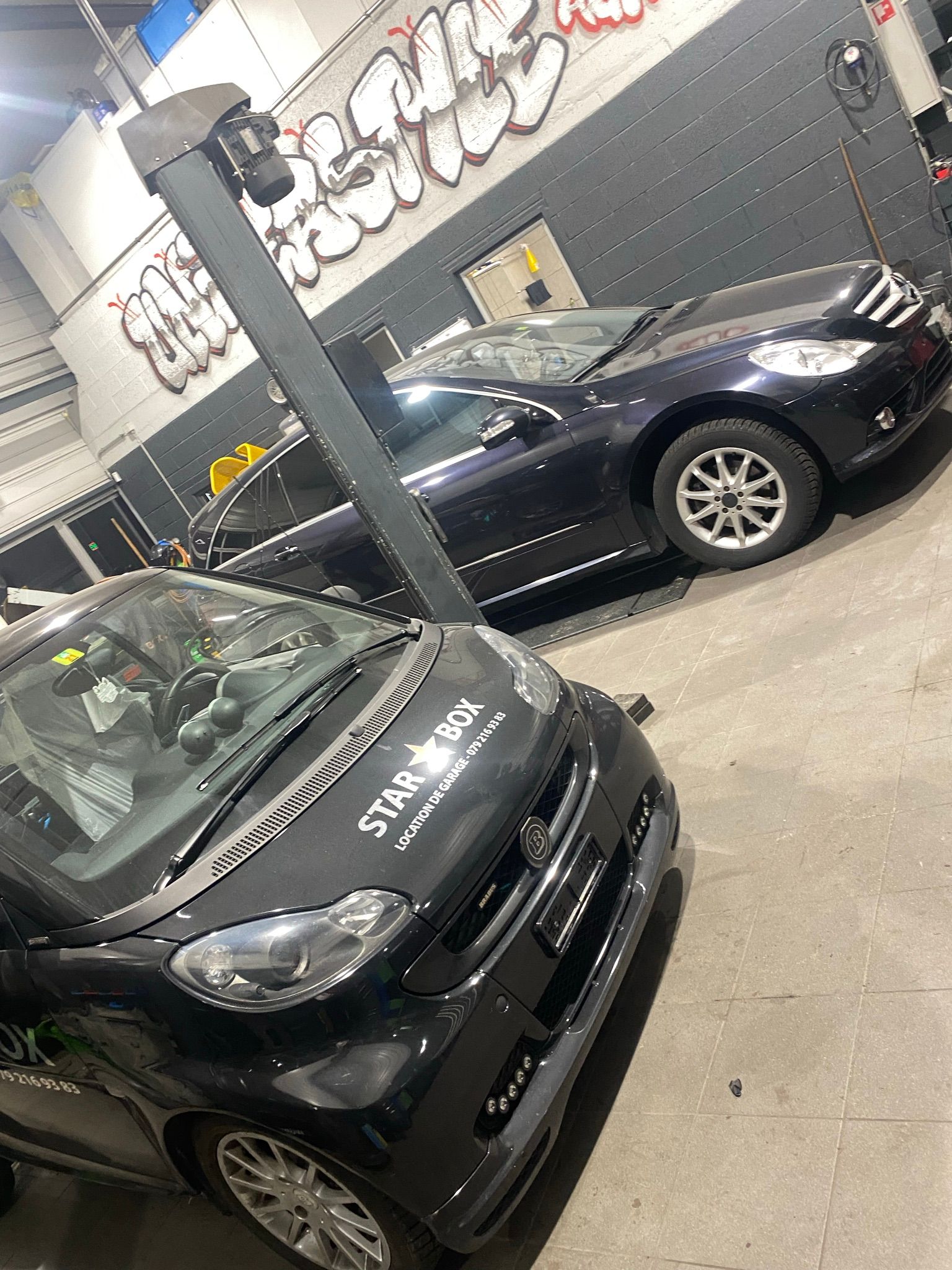 Deux voitures sont garées dans un garage avec des graffitis sur le mur.