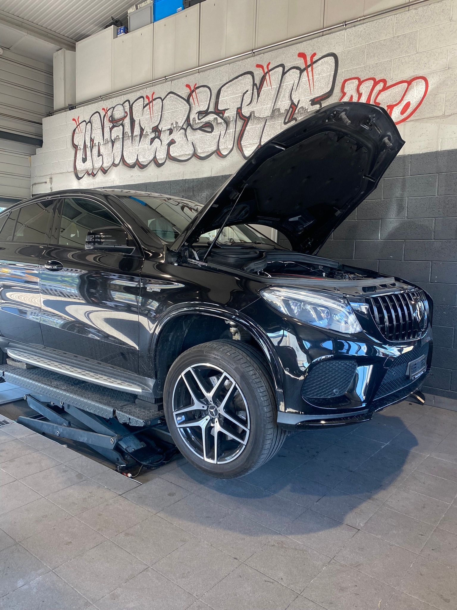Une voiture noire avec le capot relevé est garée dans un garage.