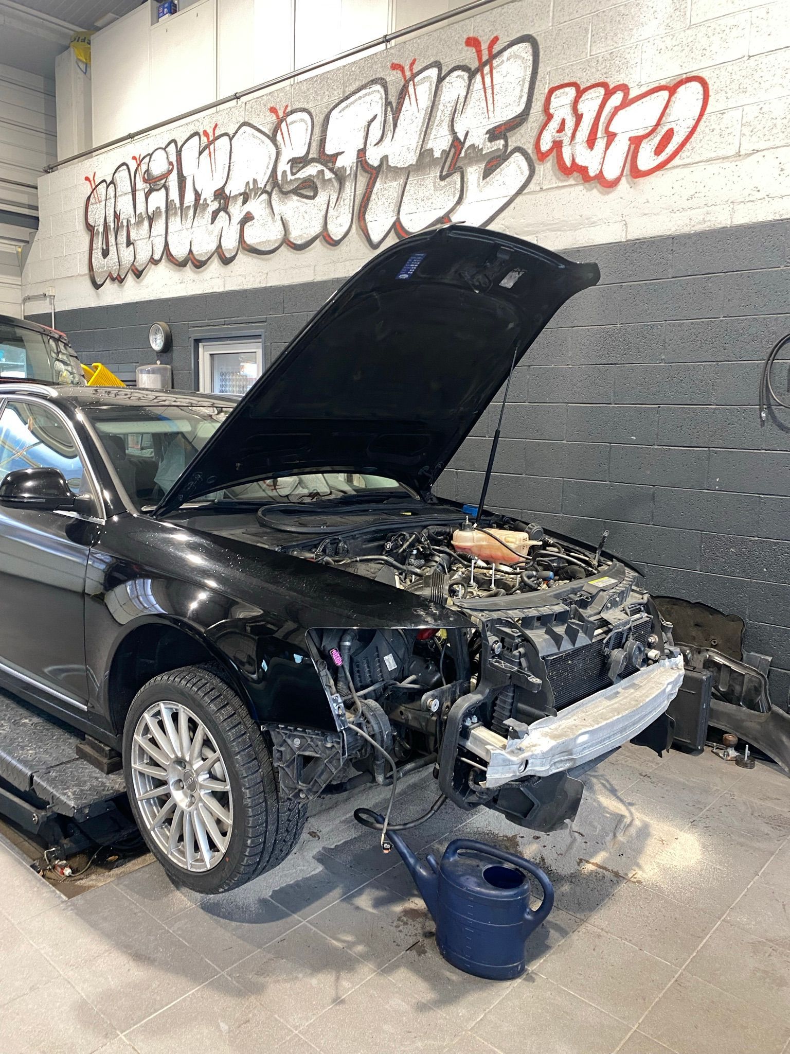 Une voiture noire avec le capot relevé est assise dans un garage.