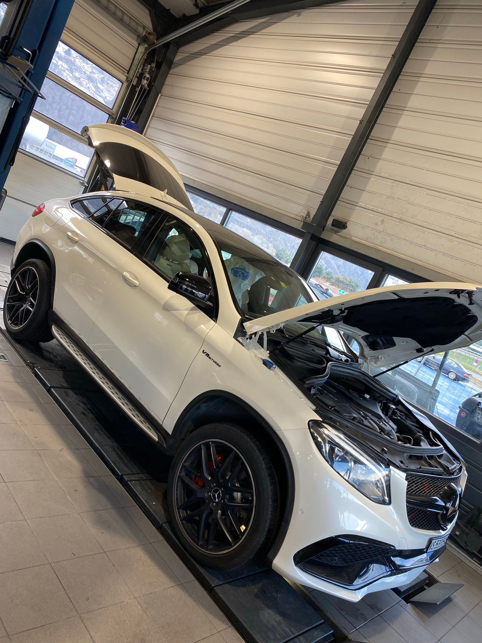 Une voiture blanche avec le capot ouvert est assise sur un ascenseur dans un garage.