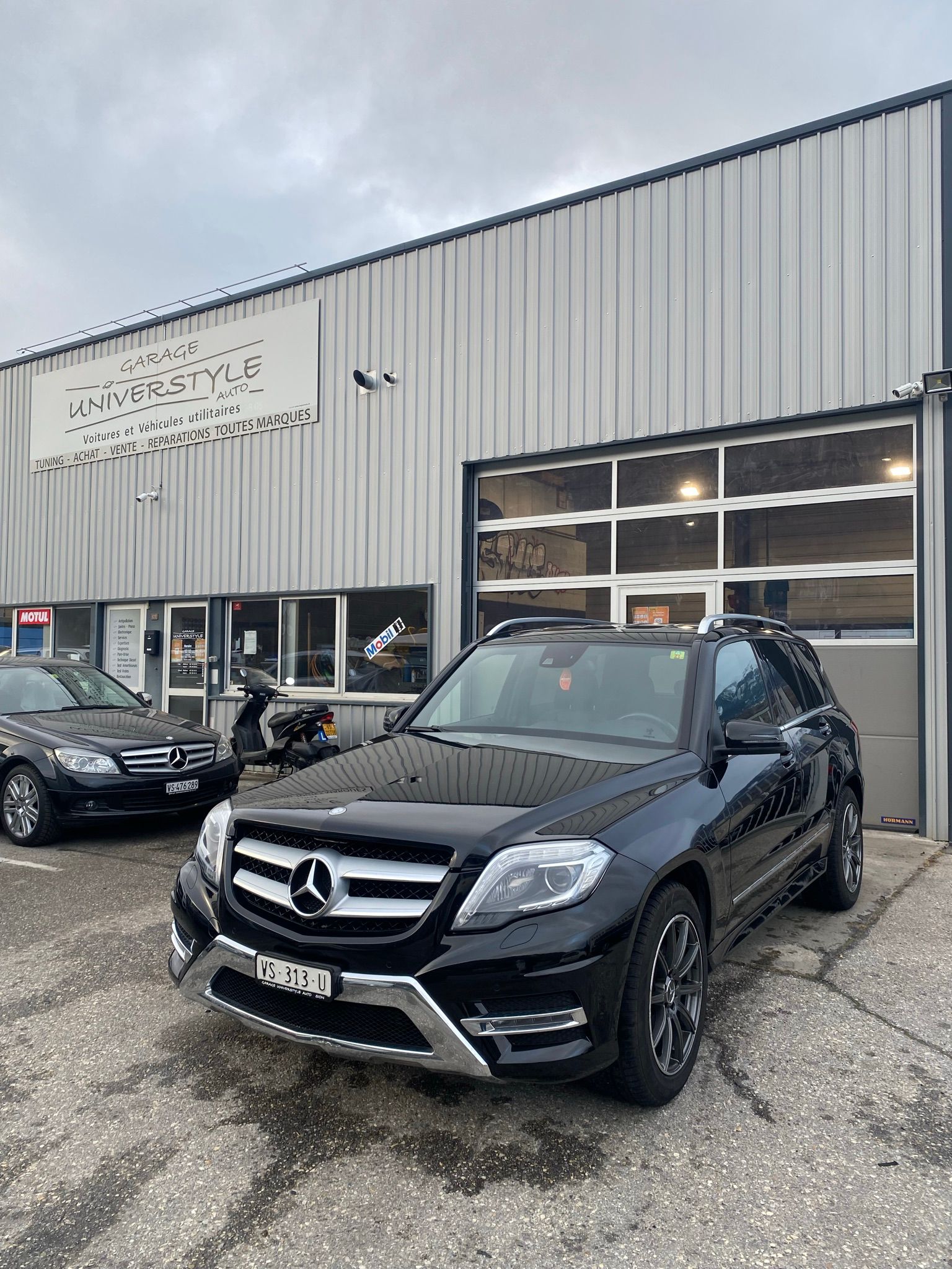 Une Mercedes Benz Glk noire est garée devant un immeuble.