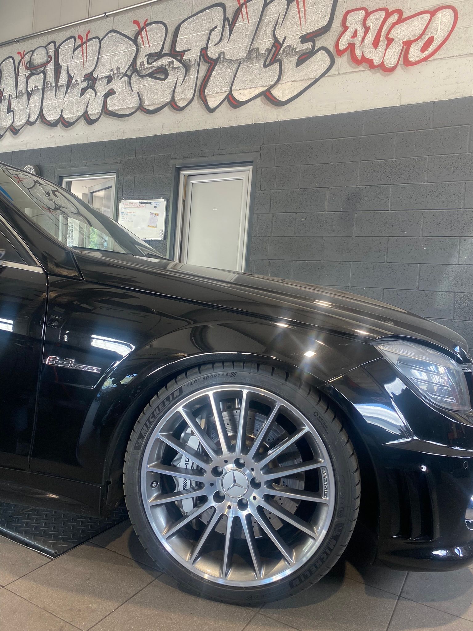 Une voiture noire est garée devant un mur avec des graffitis dessus.