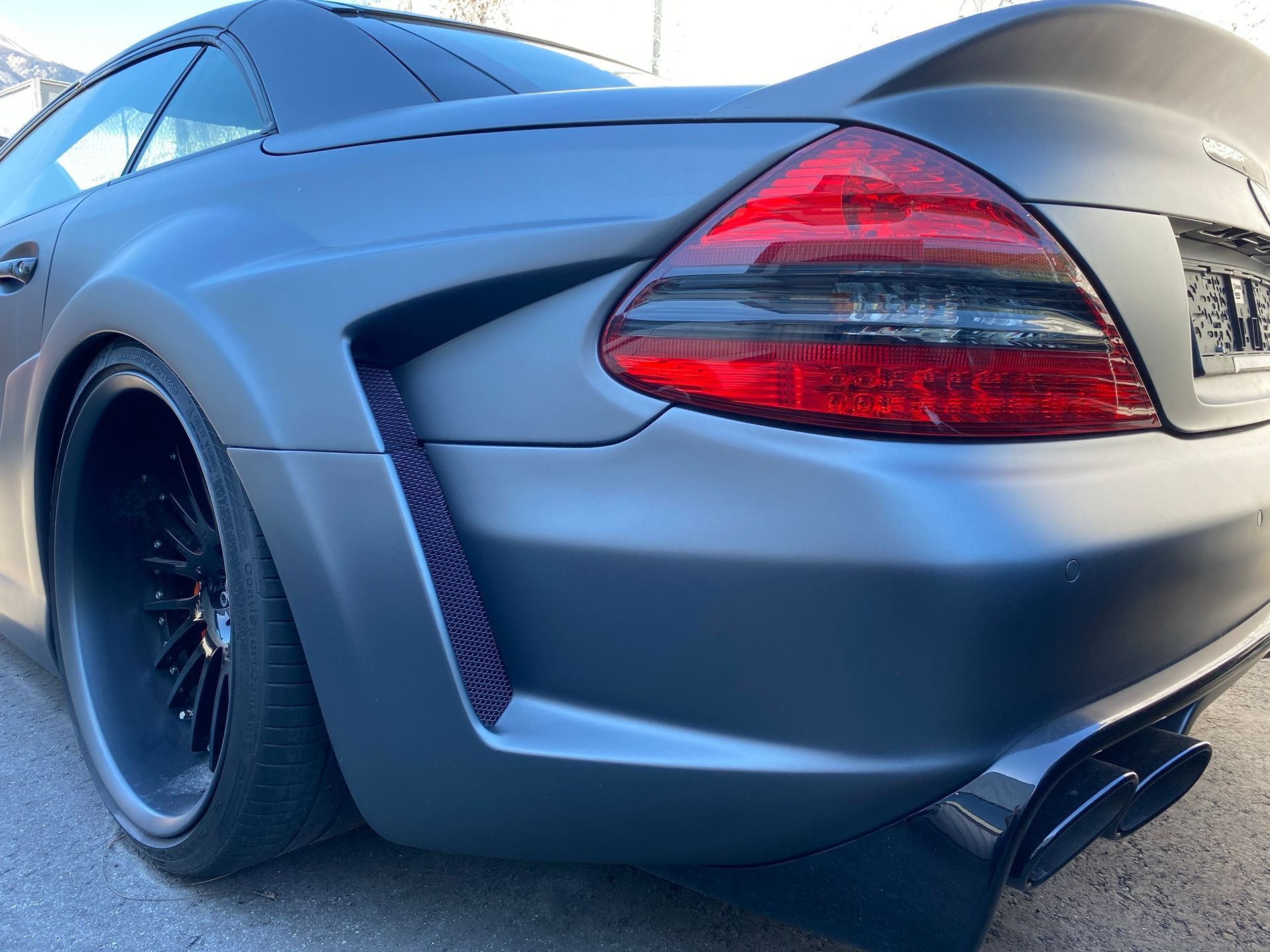 Une voiture de sport noire avec un feu arrière rouge est garée sur le bord de la route.