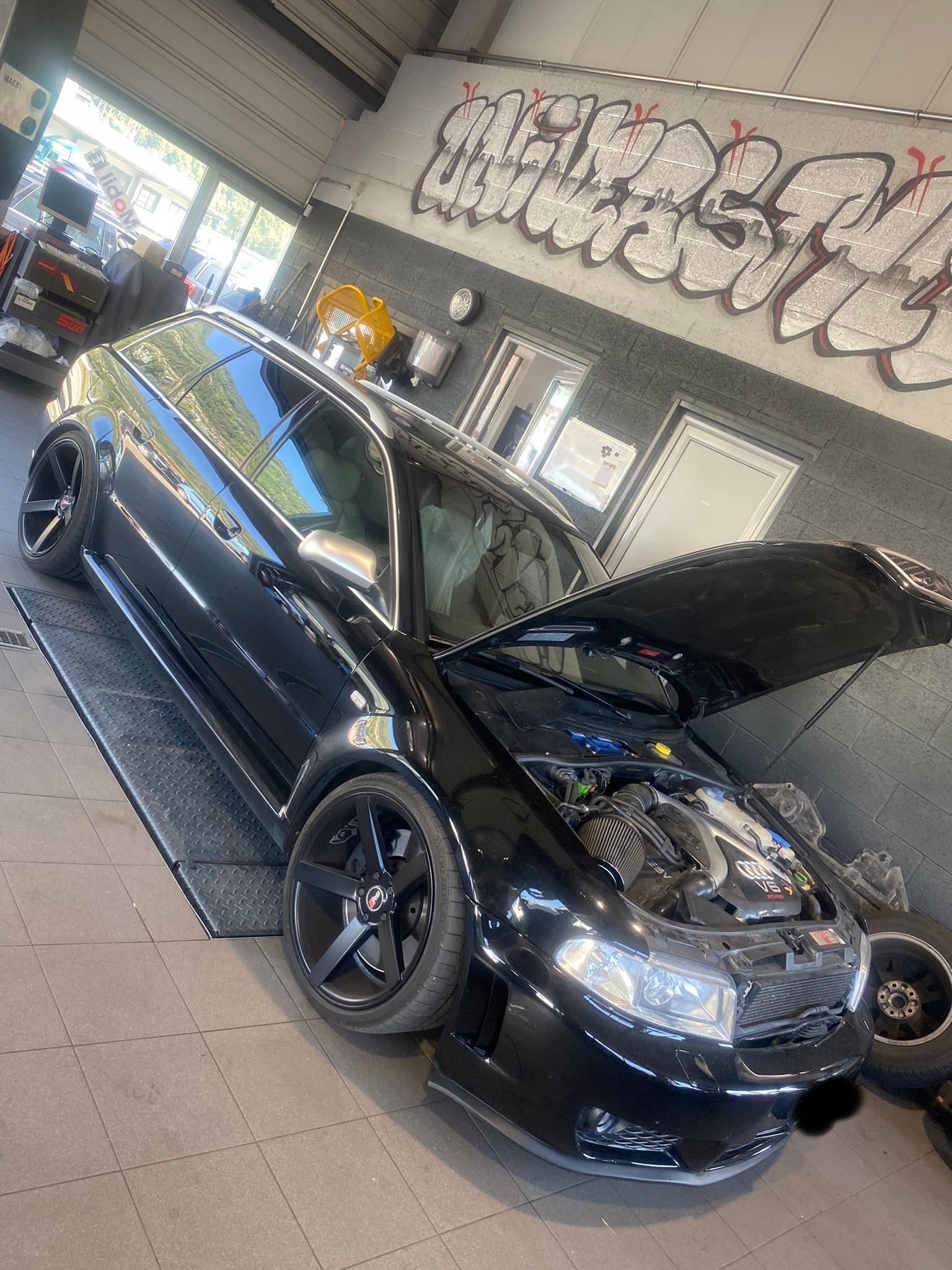 Une voiture noire avec le capot relevé est garée dans un garage.
