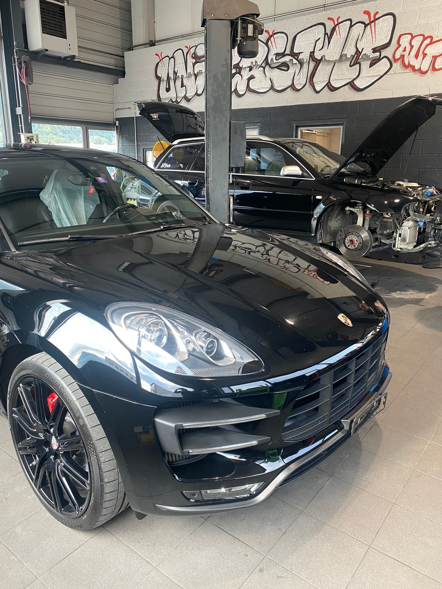 Une Porsche Macan Turbo noire est garée dans un garage avec son capot relevé.