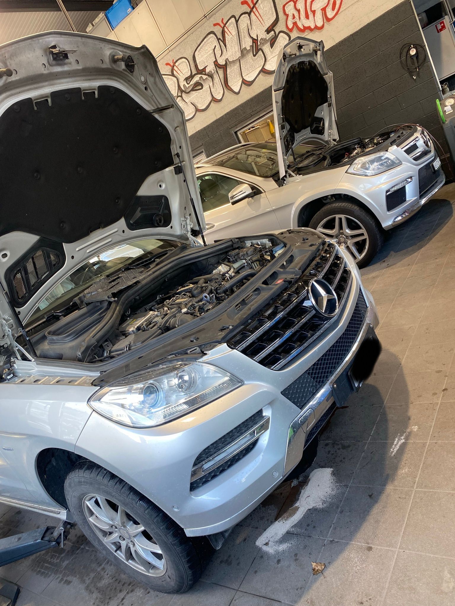 Une voiture argentée avec le capot ouvert est garée dans un garage.