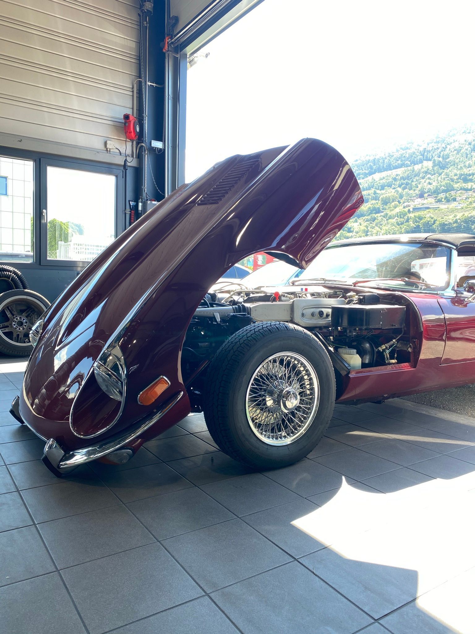 Une voiture rouge avec le capot relevé est garée dans un garage.