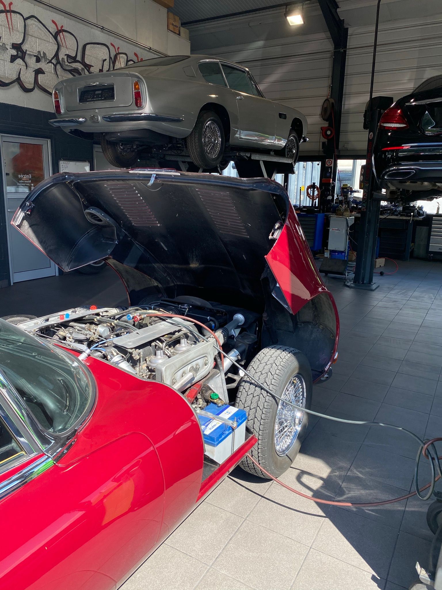 Une voiture rouge est garée dans un garage avec le capot ouvert.
