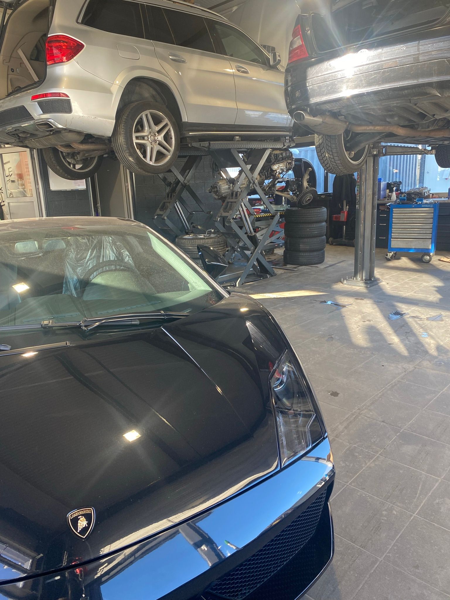 Une voiture noire est garée à côté d’un SUV argenté dans un garage.