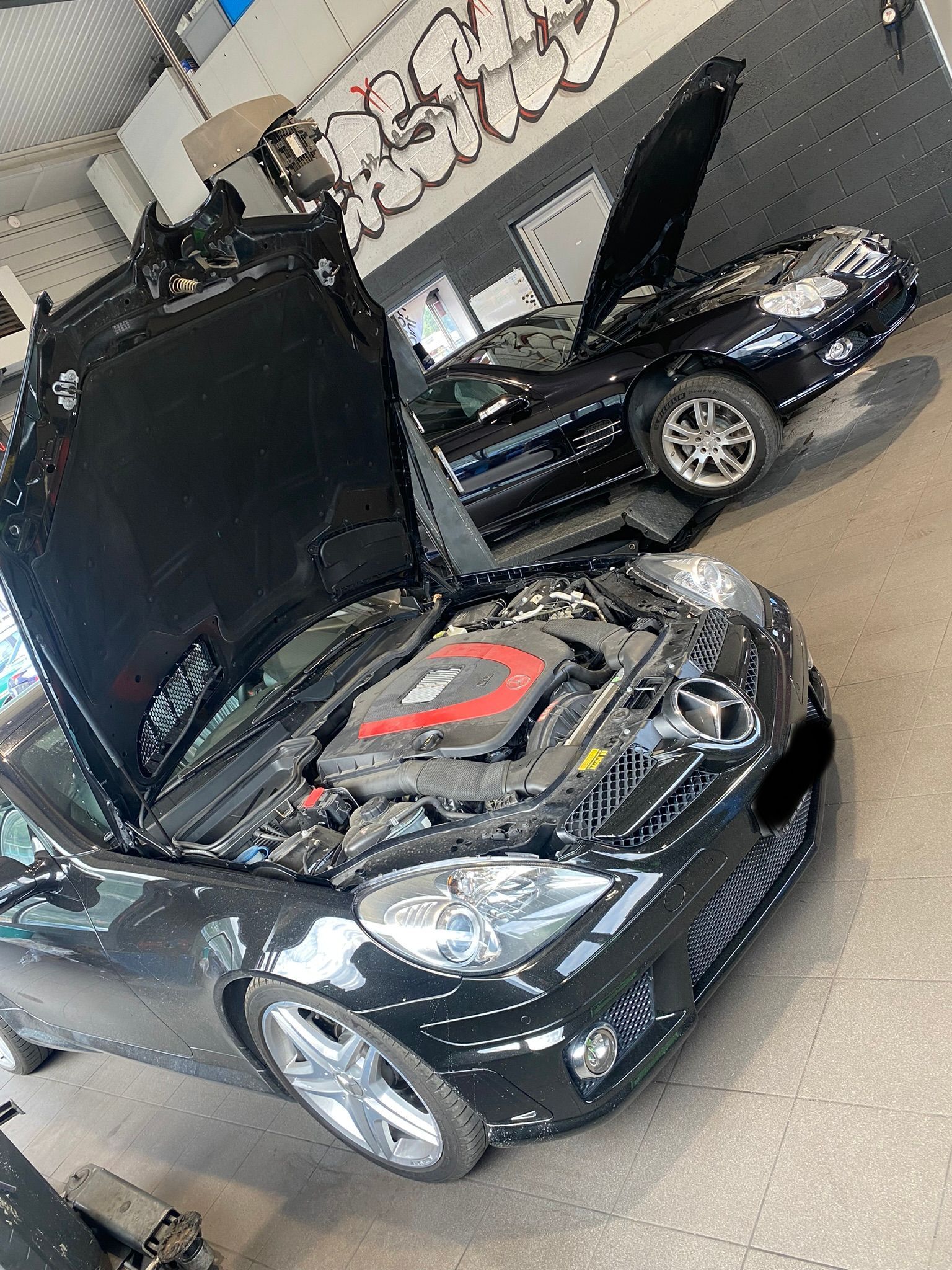 Une voiture noire avec le capot ouvert est garée dans un garage.