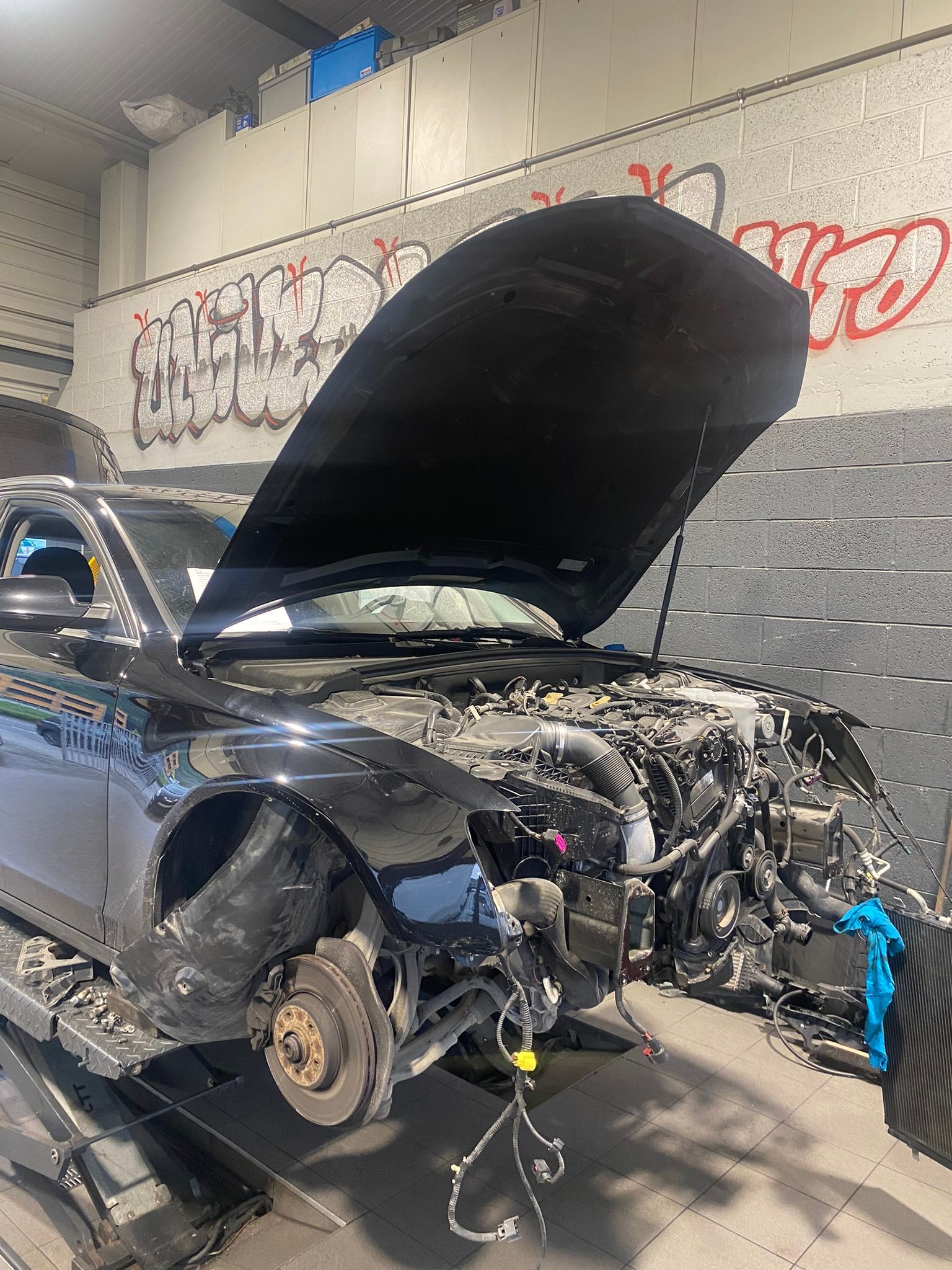 Une voiture avec le capot ouvert est assise sur un ascenseur dans un garage.