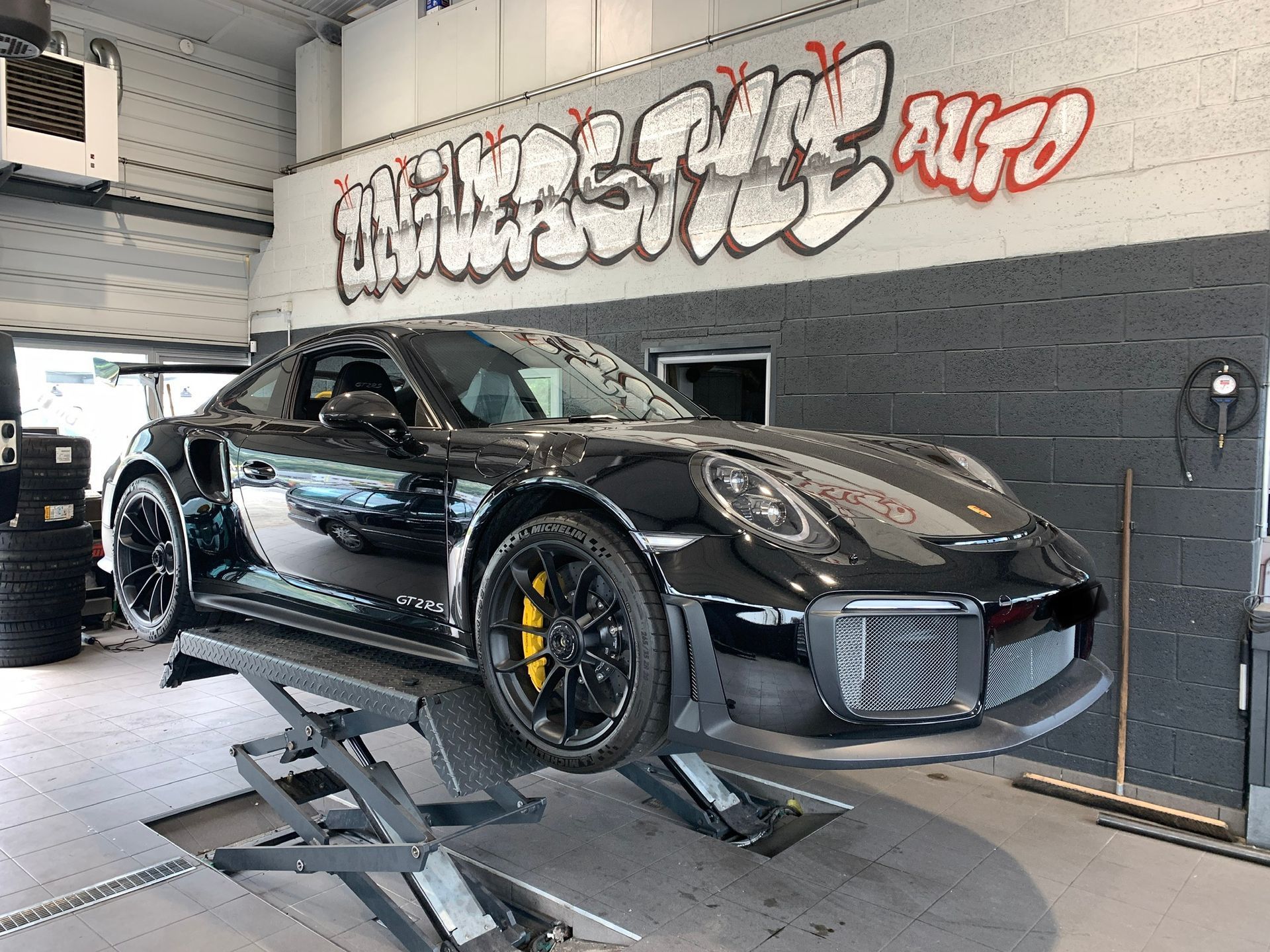 Une voiture est posée sur un ascenseur dans un garage avec des graffitis sur le mur.