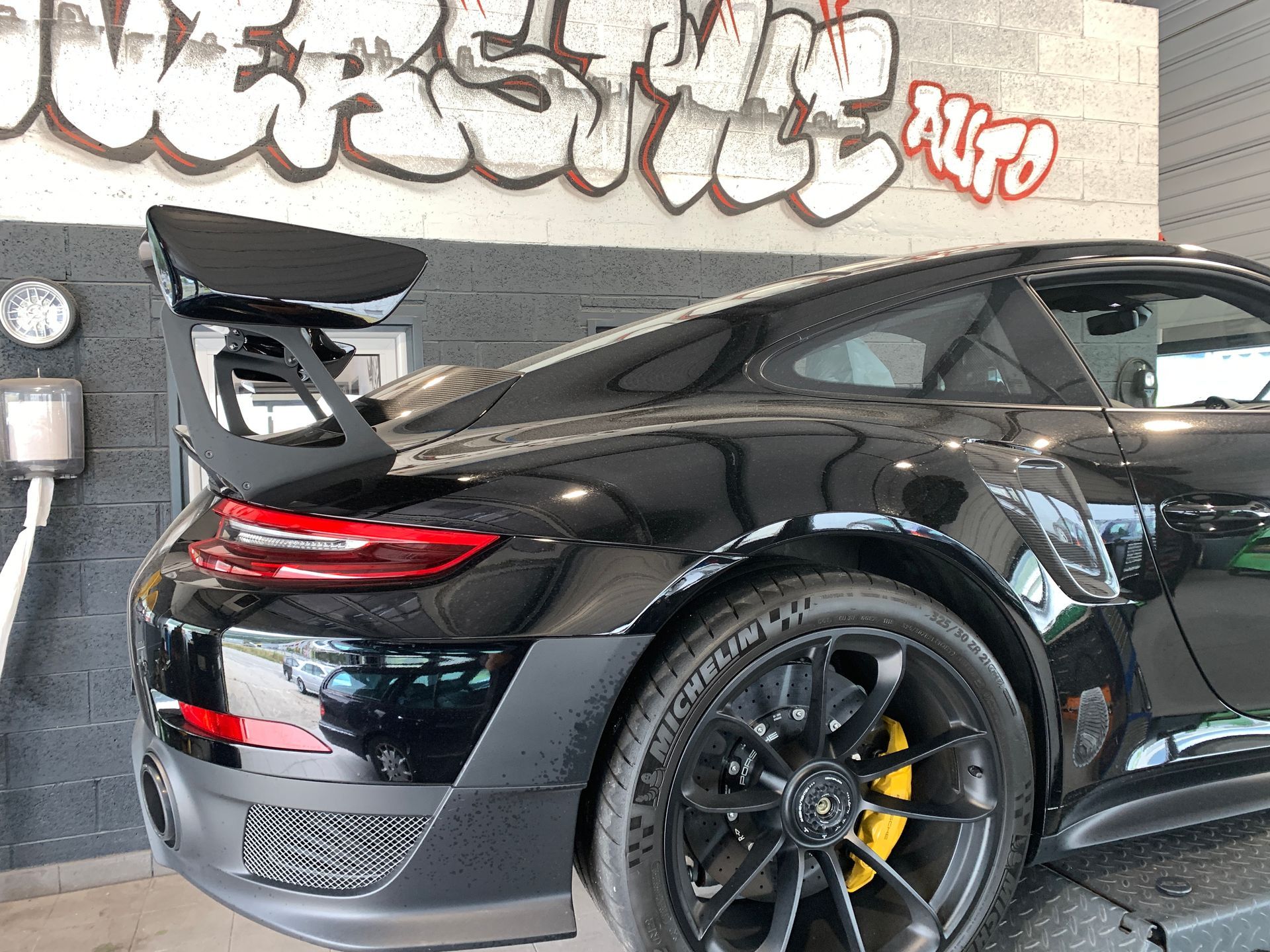 Une porsche 911 gt3 rs noire est garée devant un mur avec des graffitis dessus.