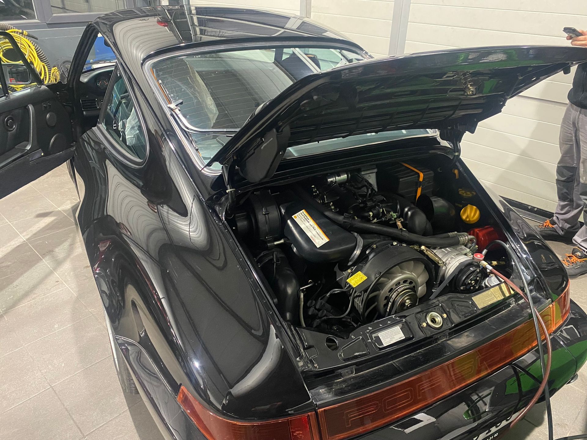Un homme travaille sur le moteur d’une Porsche noire avec le capot ouvert.