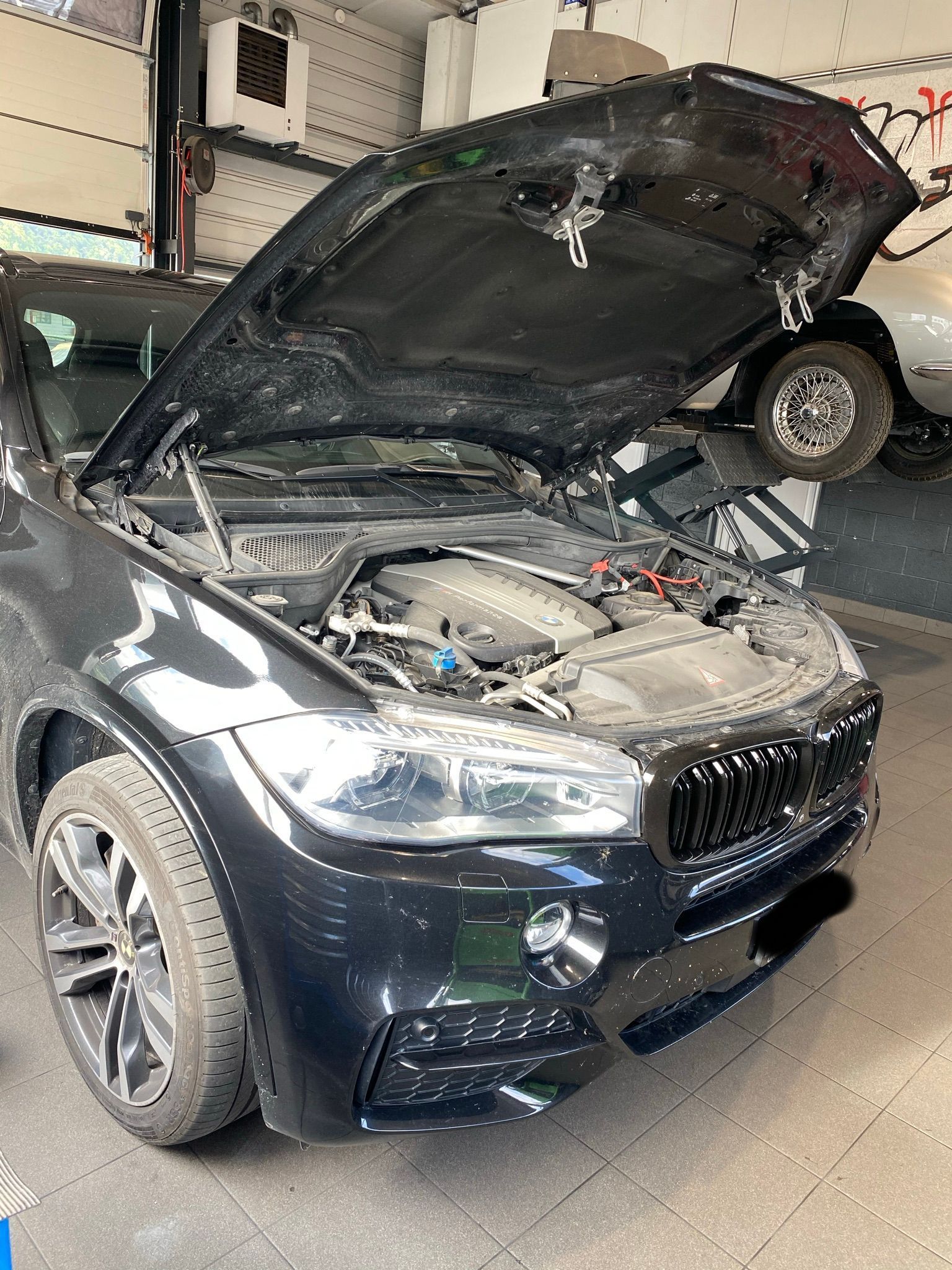 Une BMW X5 noire avec le capot relevé dans un garage.
