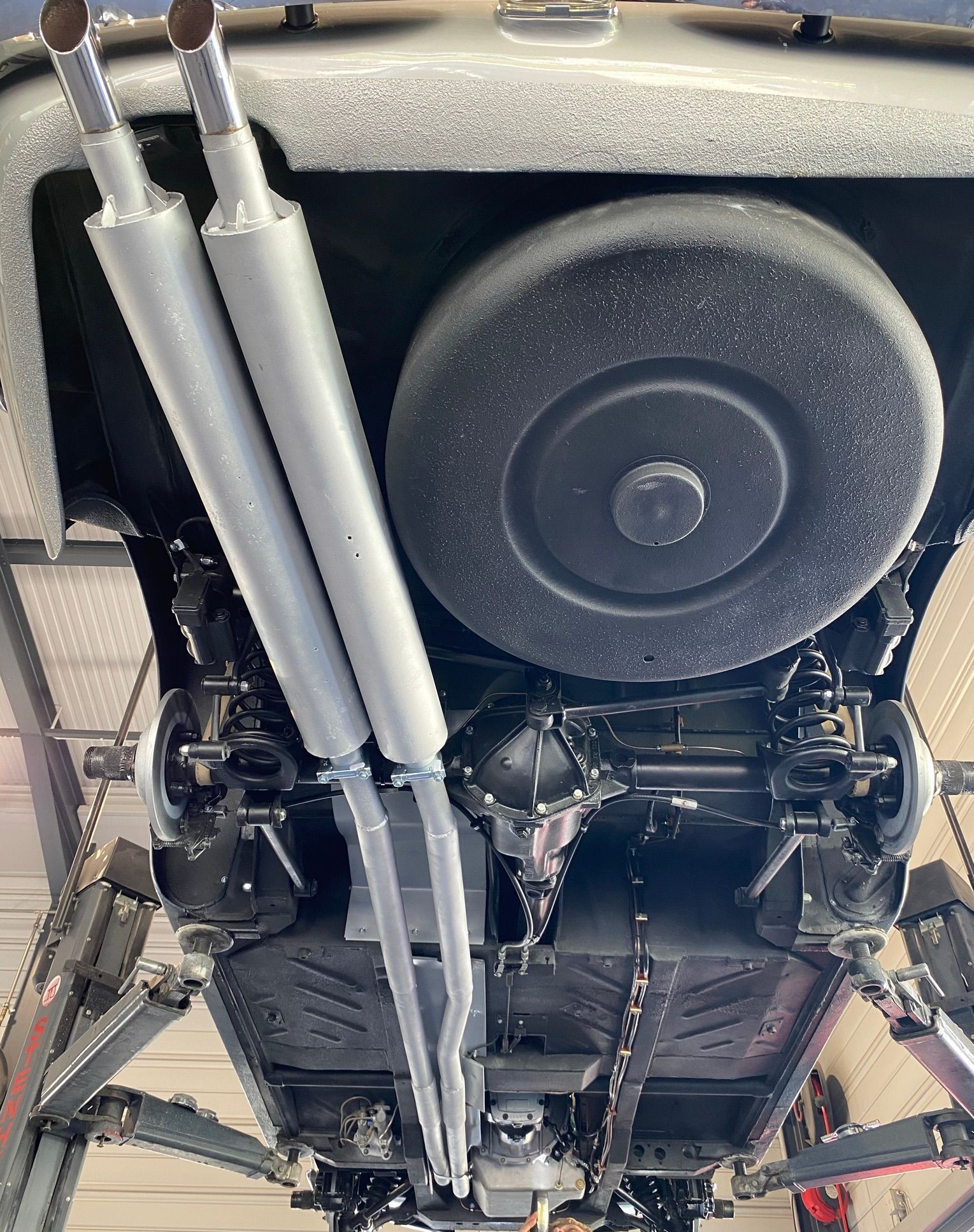 Le dessous d’une voiture avec des pots d’échappement et un pneu.