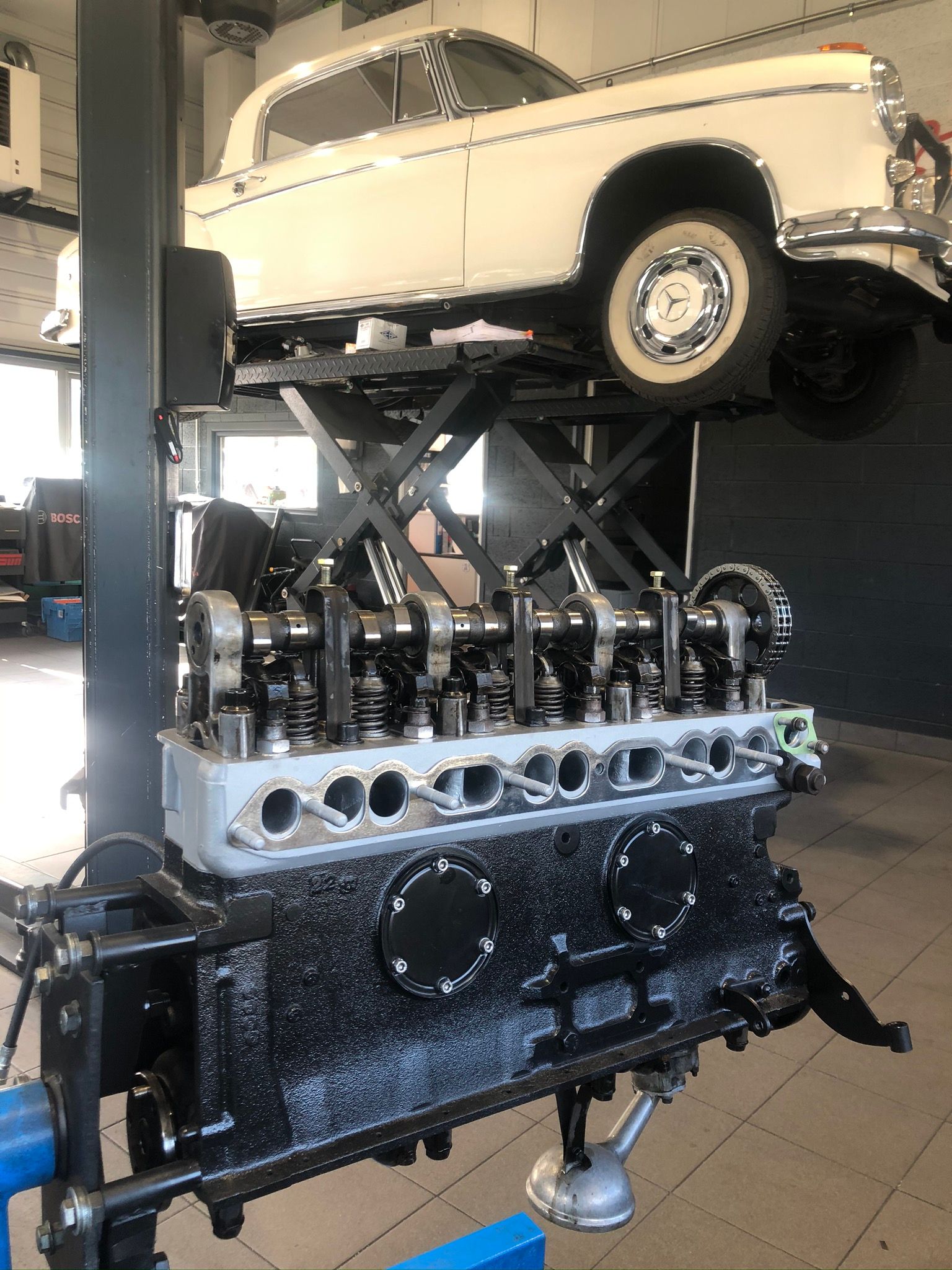 Une voiture blanche est posée sur un moteur noir dans un garage.