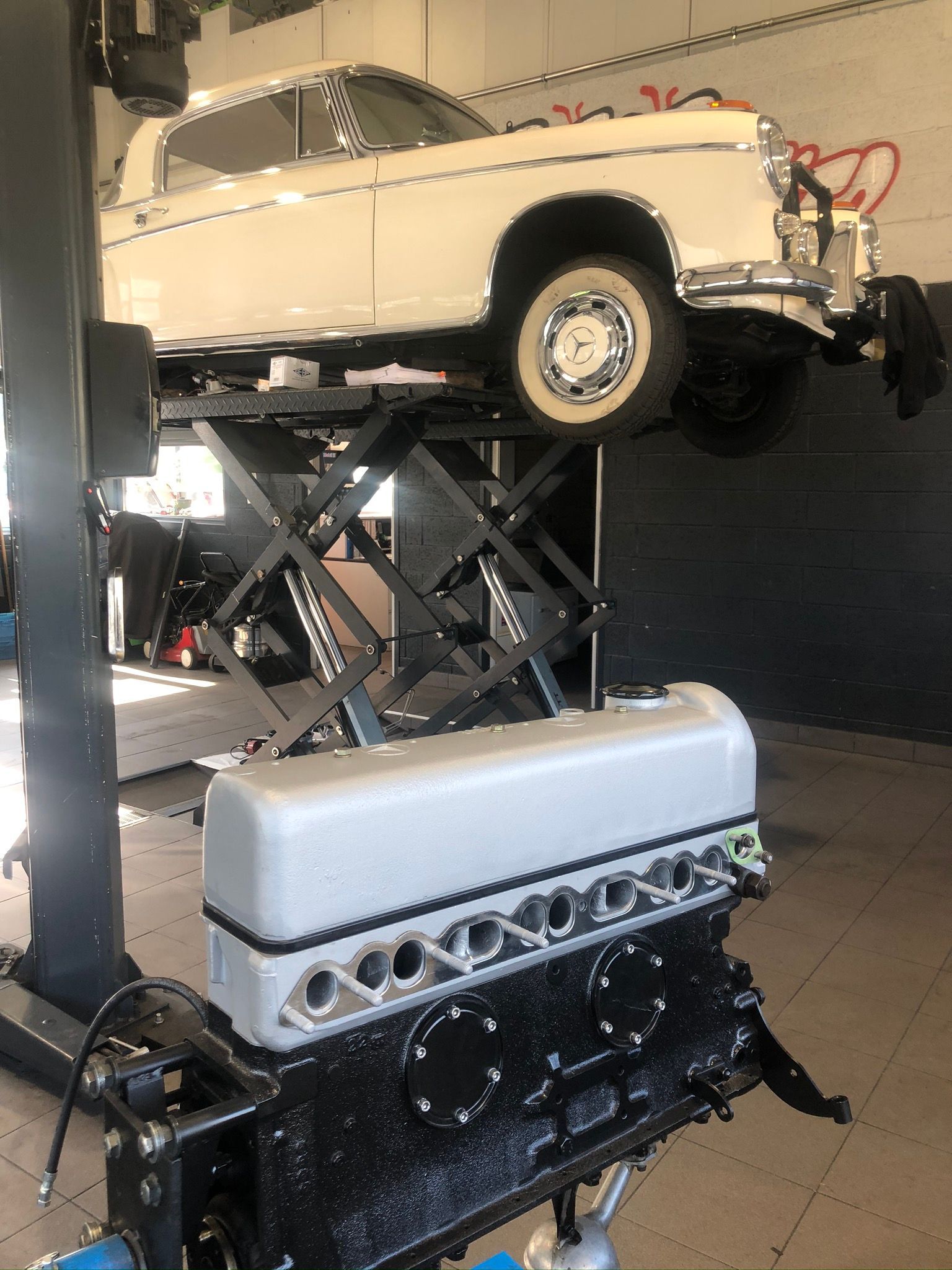 Une voiture blanche est assise sur un ascenseur à côté d’un moteur noir.