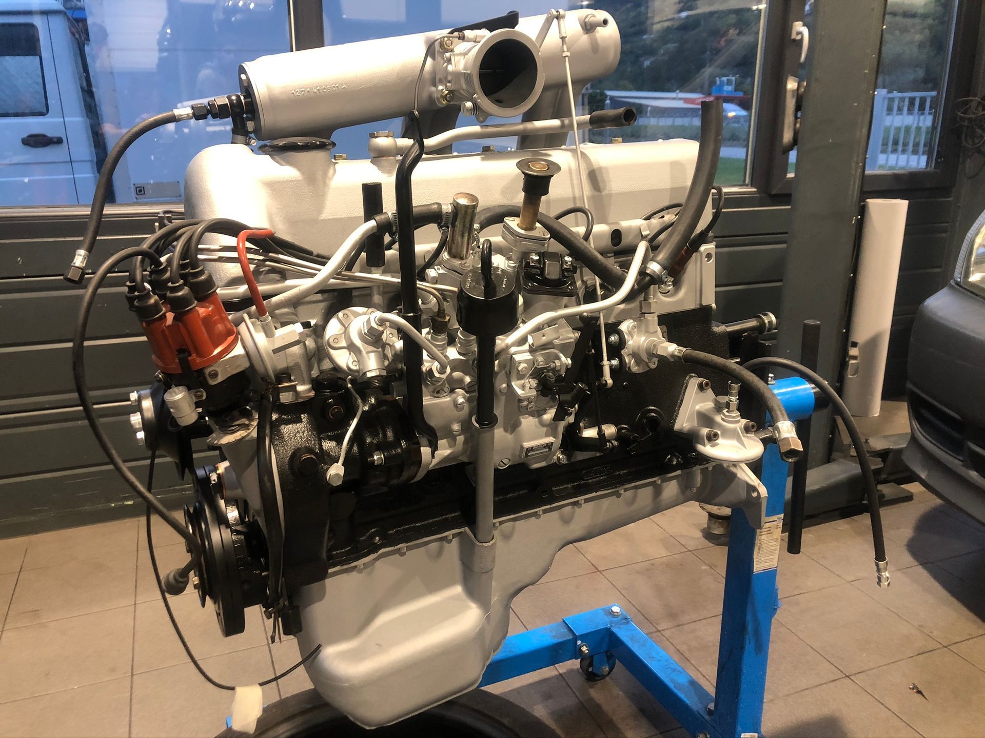 Un moteur de voiture est posé sur un support bleu dans un garage.