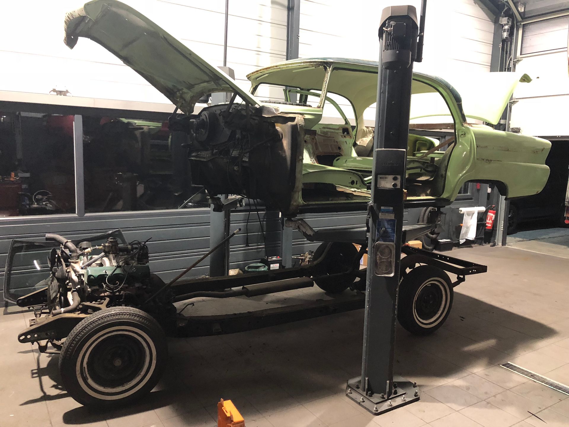 Une voiture verte avec le capot relevé est assise sur un ascenseur dans un garage.