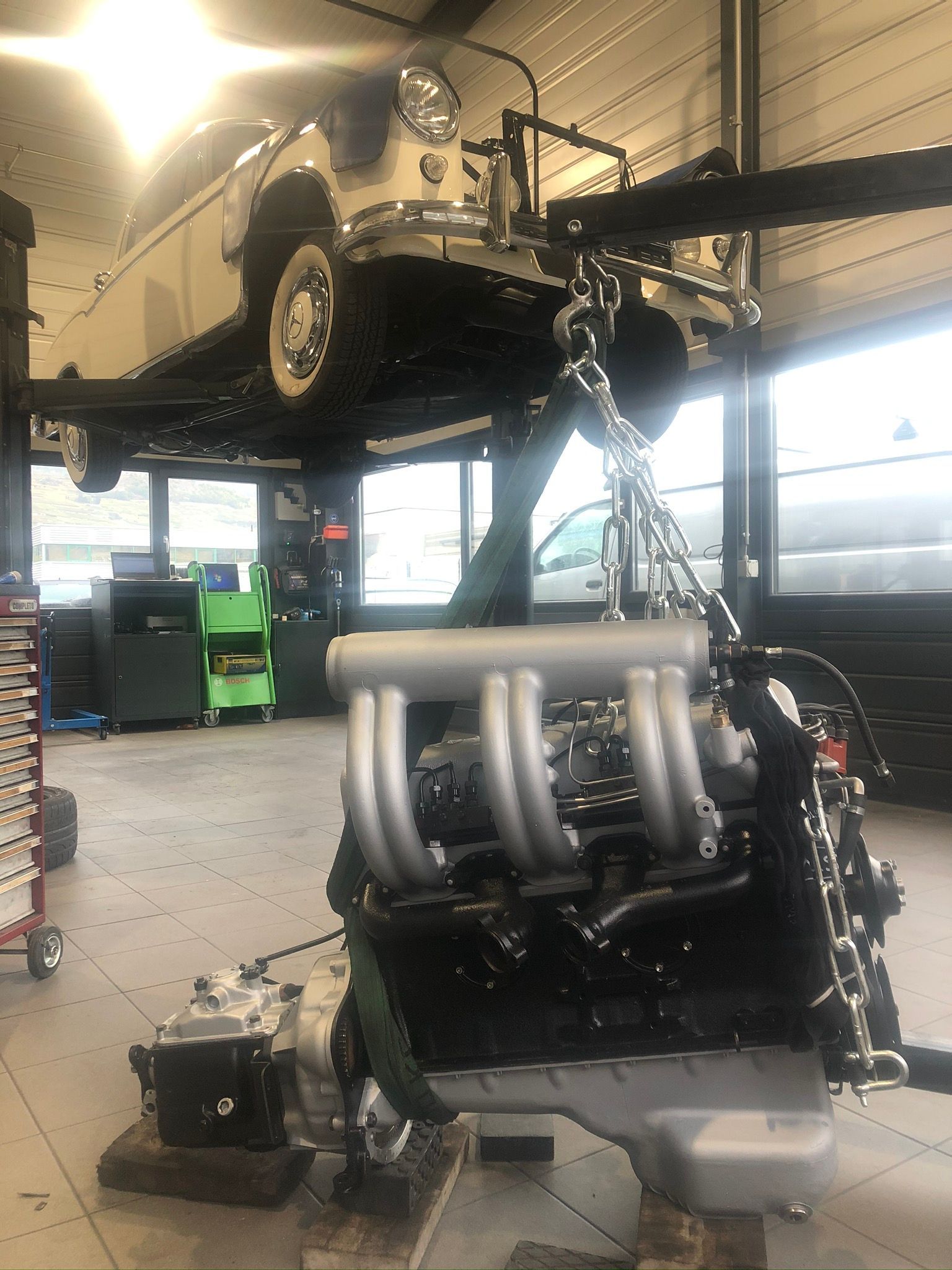 Un moteur de voiture est soulevé par une grue dans un garage.