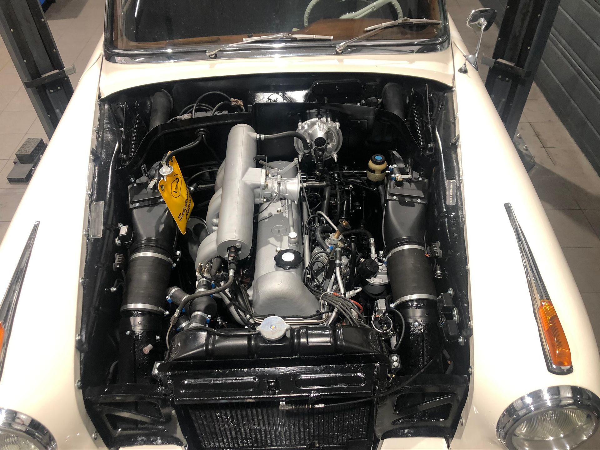 Le moteur d’une voiture blanche est visible sous le capot.