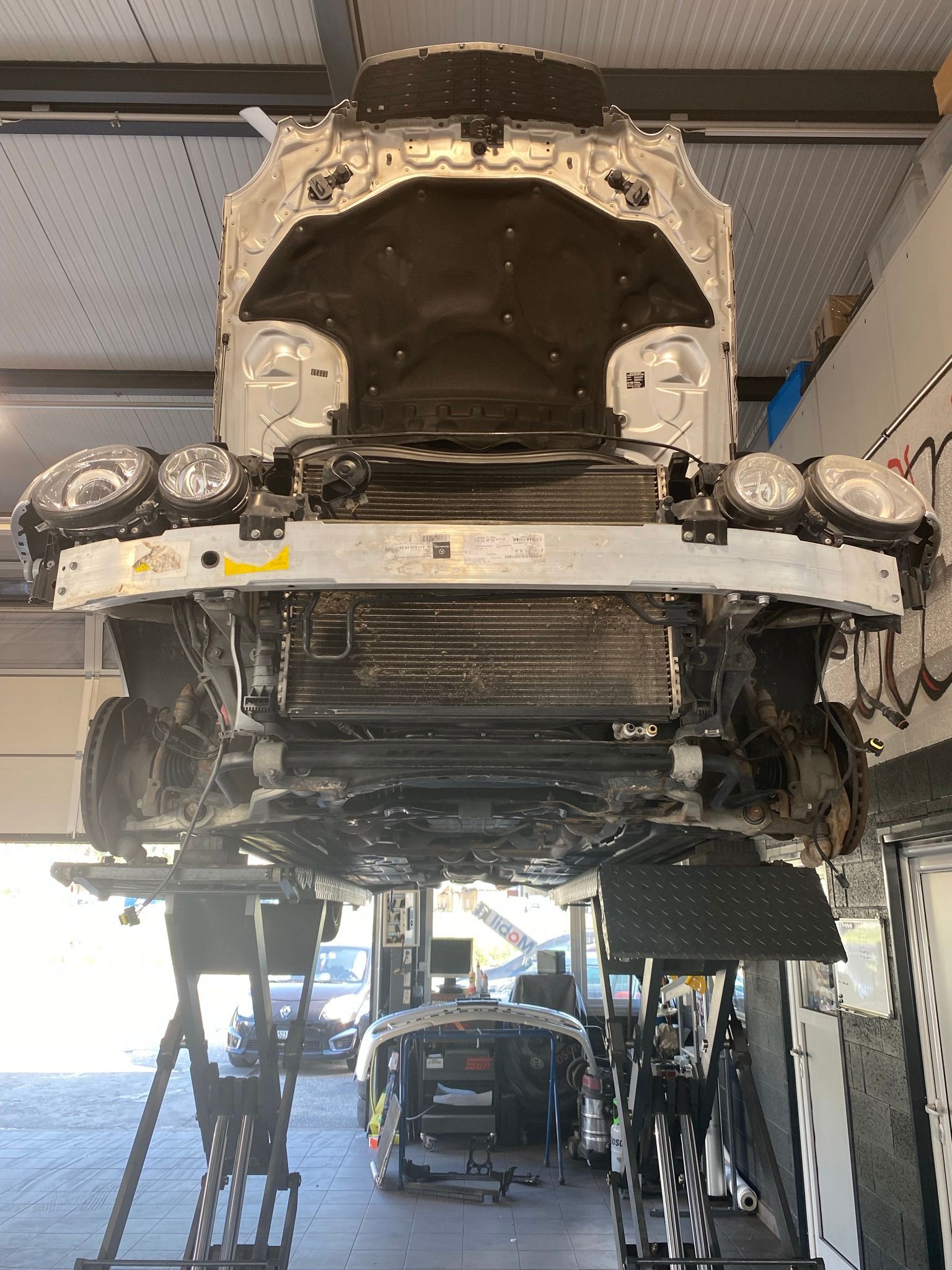 Une voiture est en réparation dans un garage avec le capot relevé.