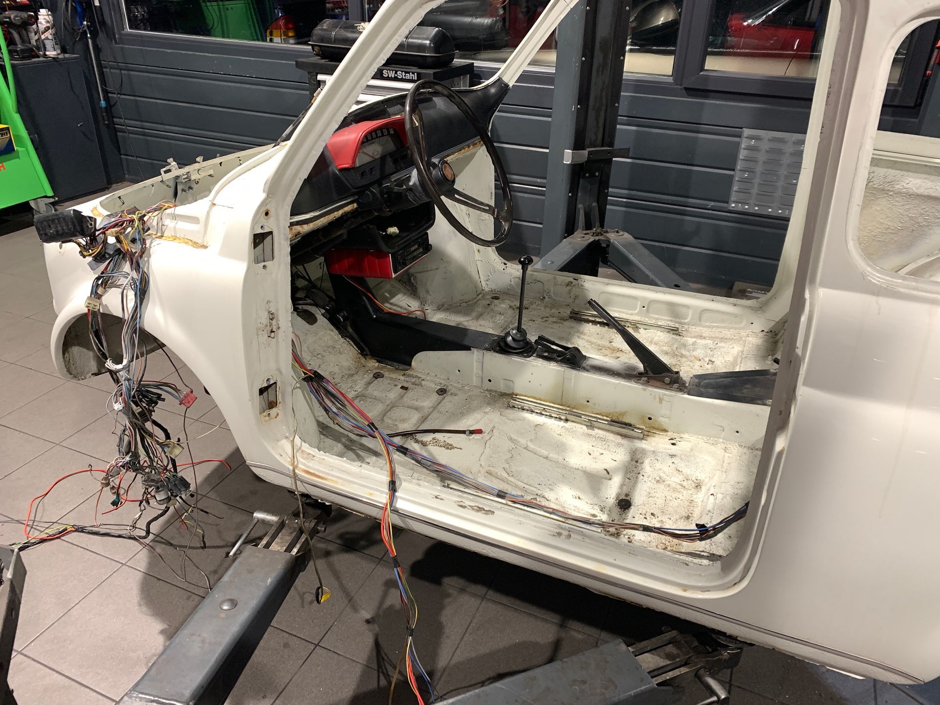 Une voiture blanche avec la porte ouverte est assise sur un ascenseur dans un garage.