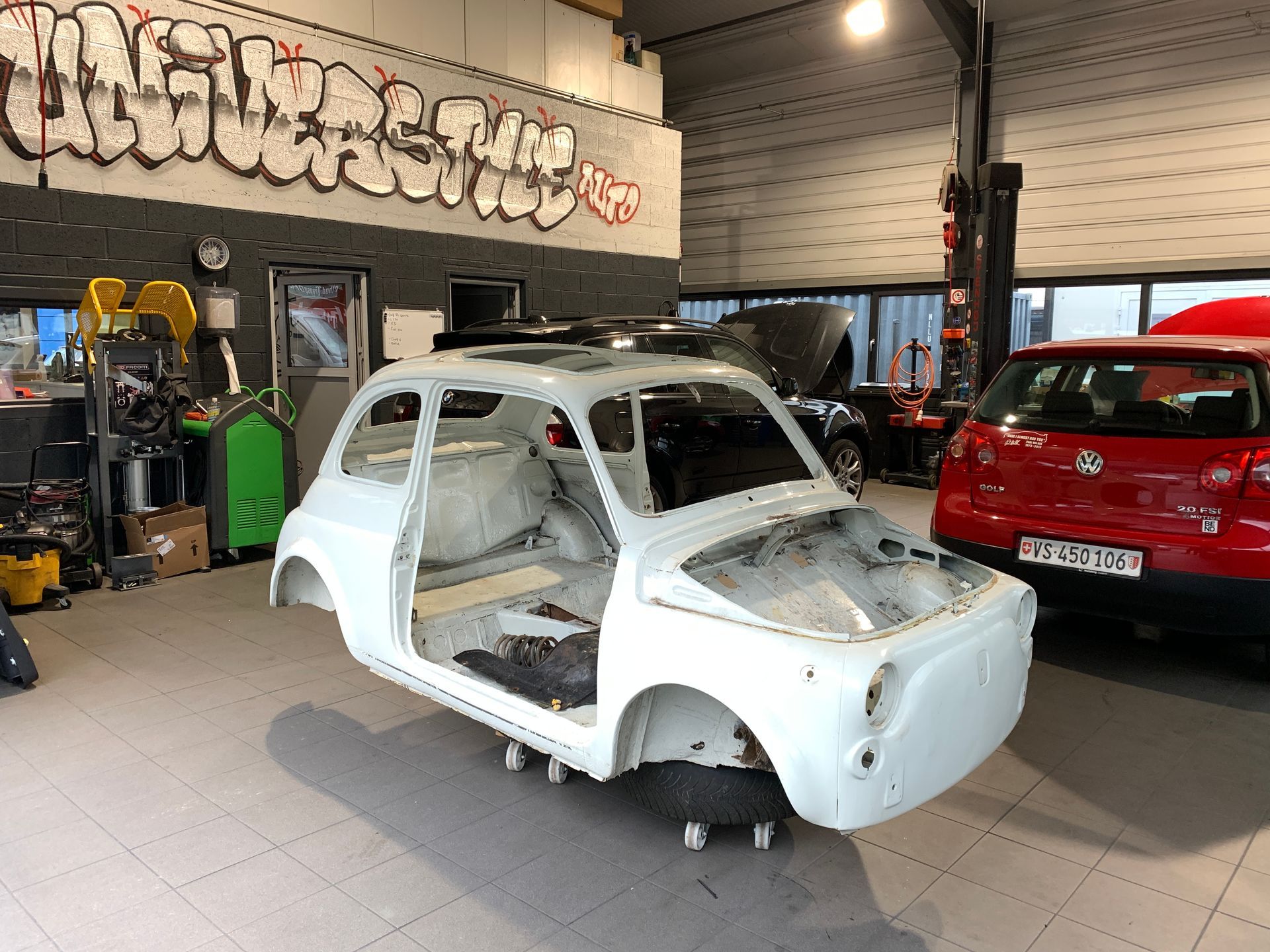 Une voiture blanche est assise dans un garage à côté d’une voiture rouge.