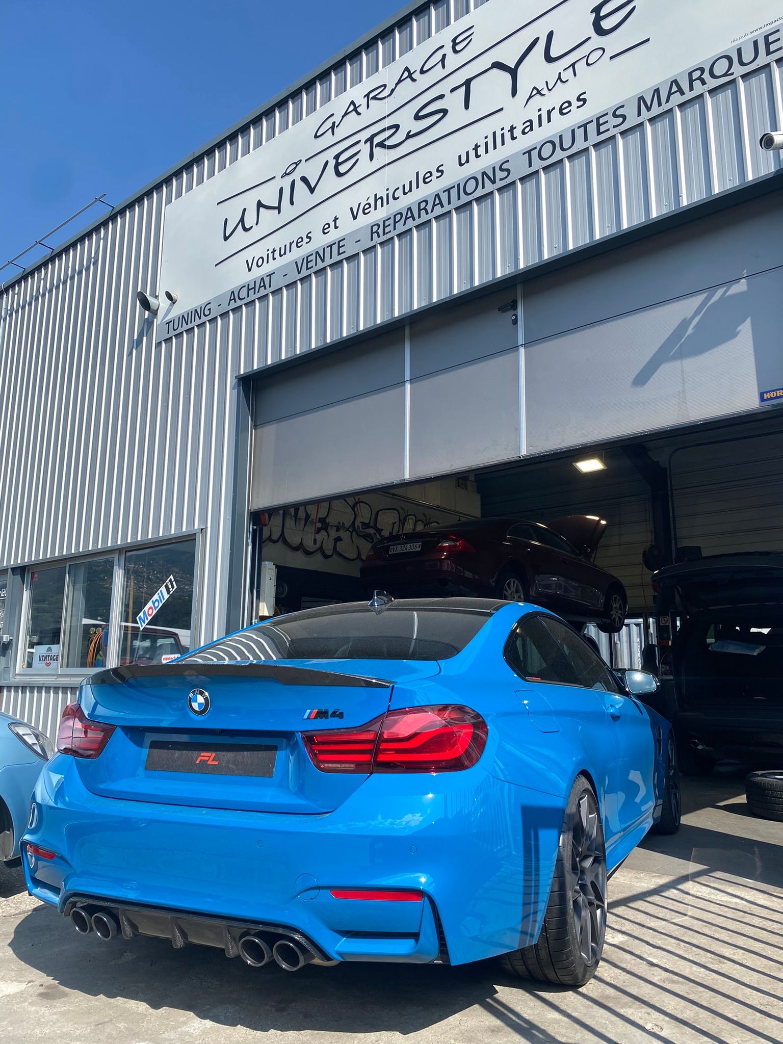 Une BMW M3 bleue est garée devant un garage.