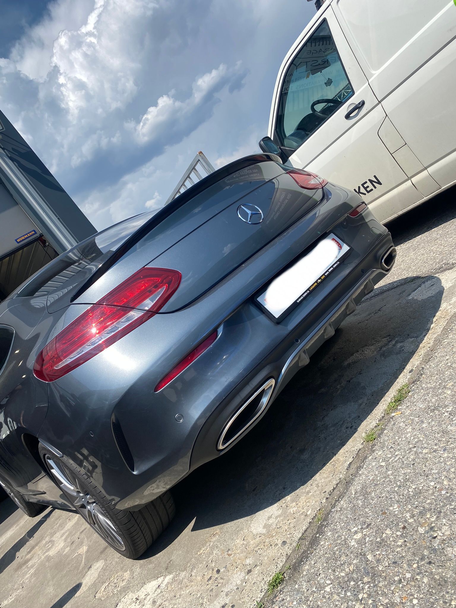 Une Mercedes Classe C est garée dans un parking à côté d'une camionnette blanche.