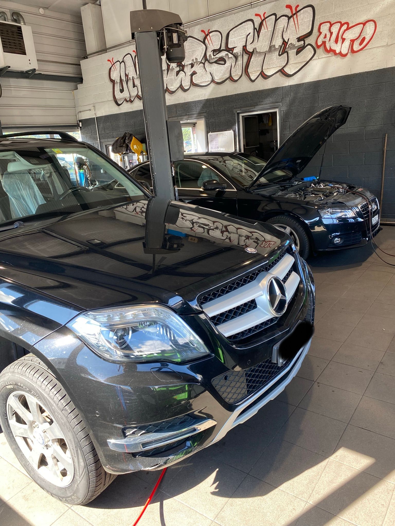 Deux voitures noires sont garées dans un garage avec des graffitis sur les murs.