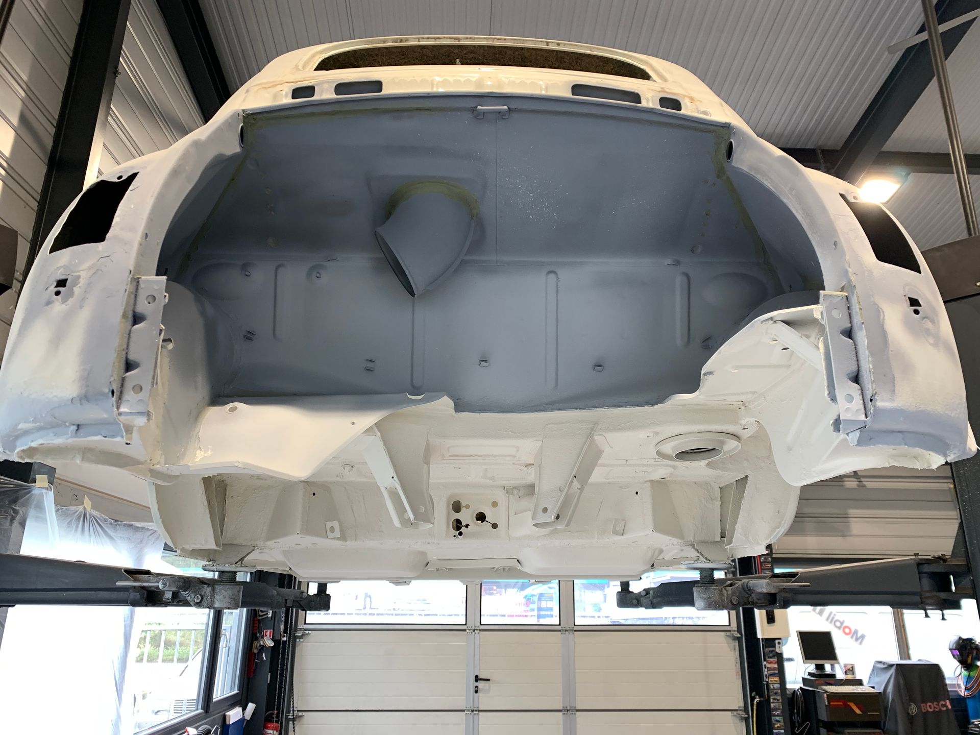 Une voiture blanche est assise sur un ascenseur dans un garage.