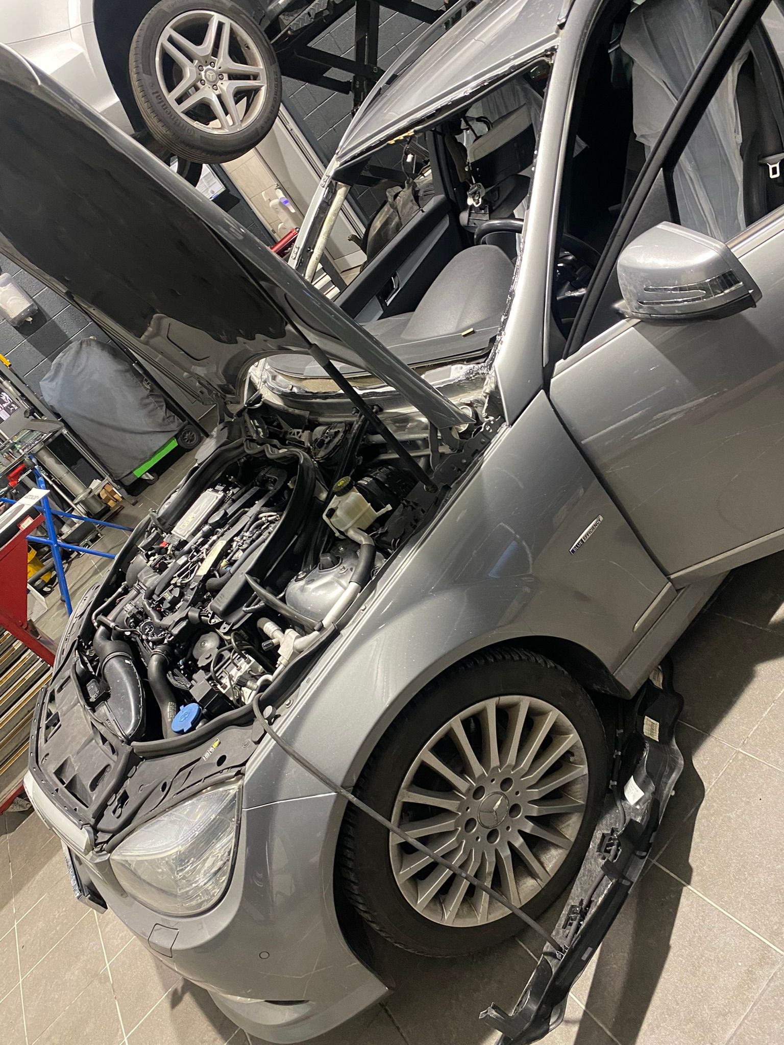 Une voiture argentée avec le capot ouvert se trouve dans un garage.