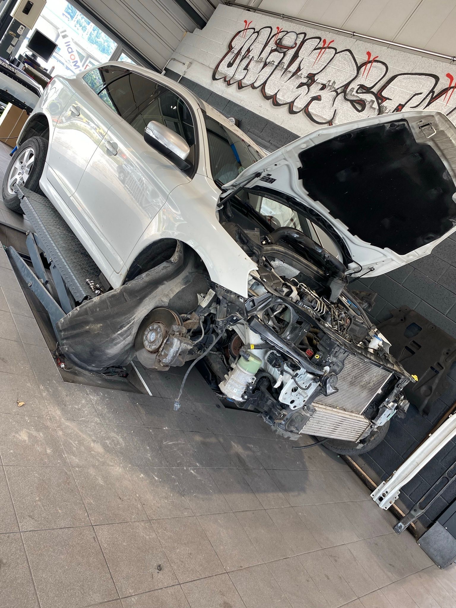 Une voiture blanche avec le capot ouvert est assise sur un ascenseur dans un garage.
