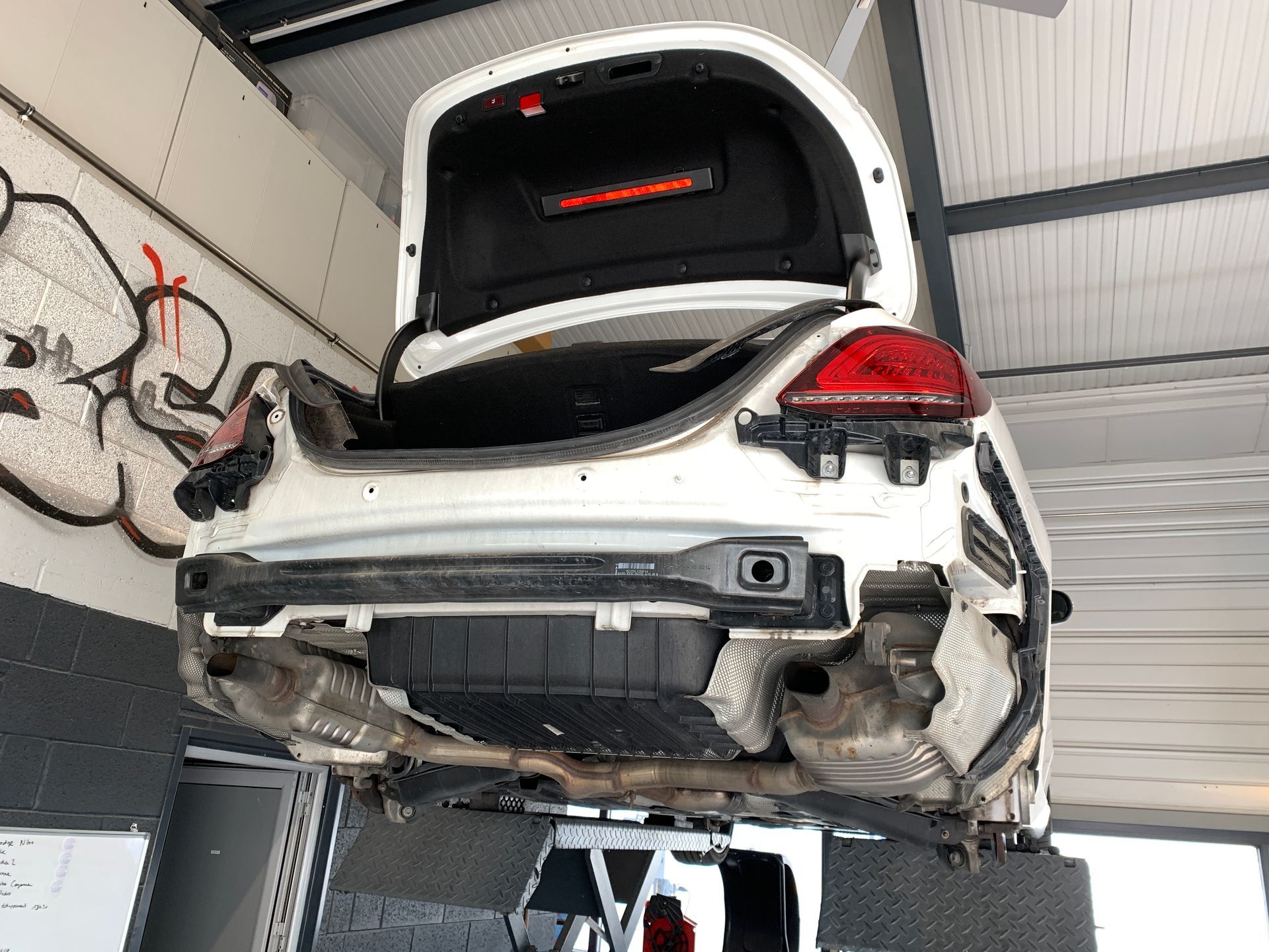 Une voiture blanche avec le coffre ouvert est assise sur un ascenseur dans un garage.