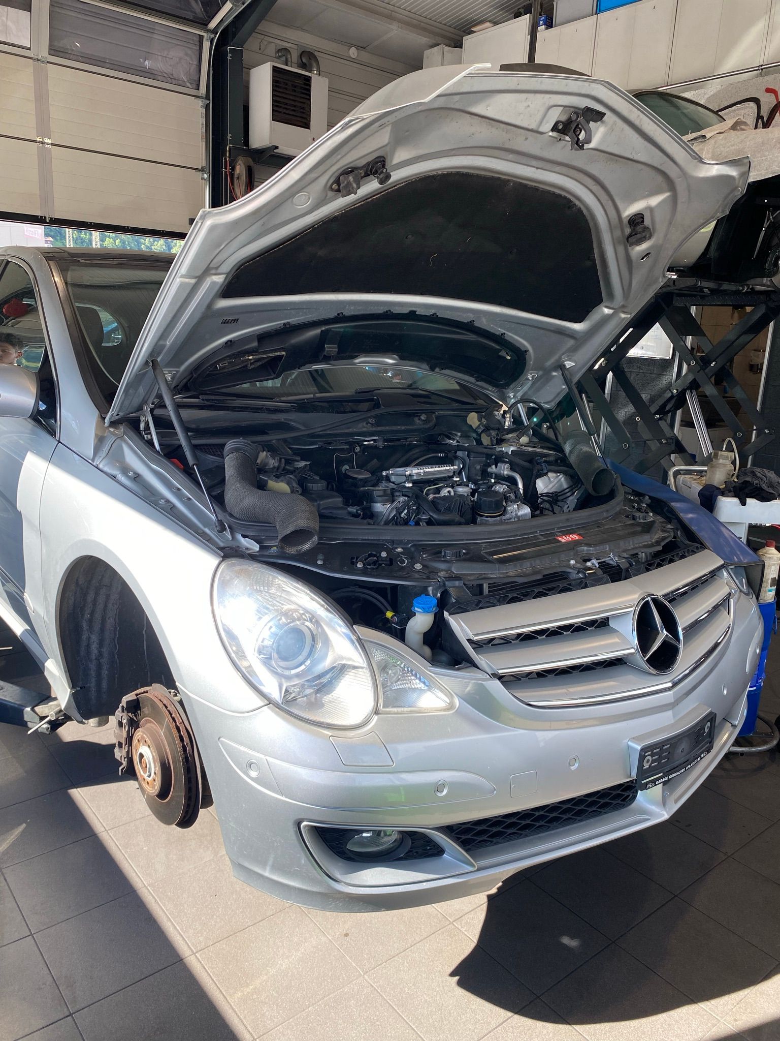 Une Mercedes Benz argentée avec le capot ouvert dans un garage.