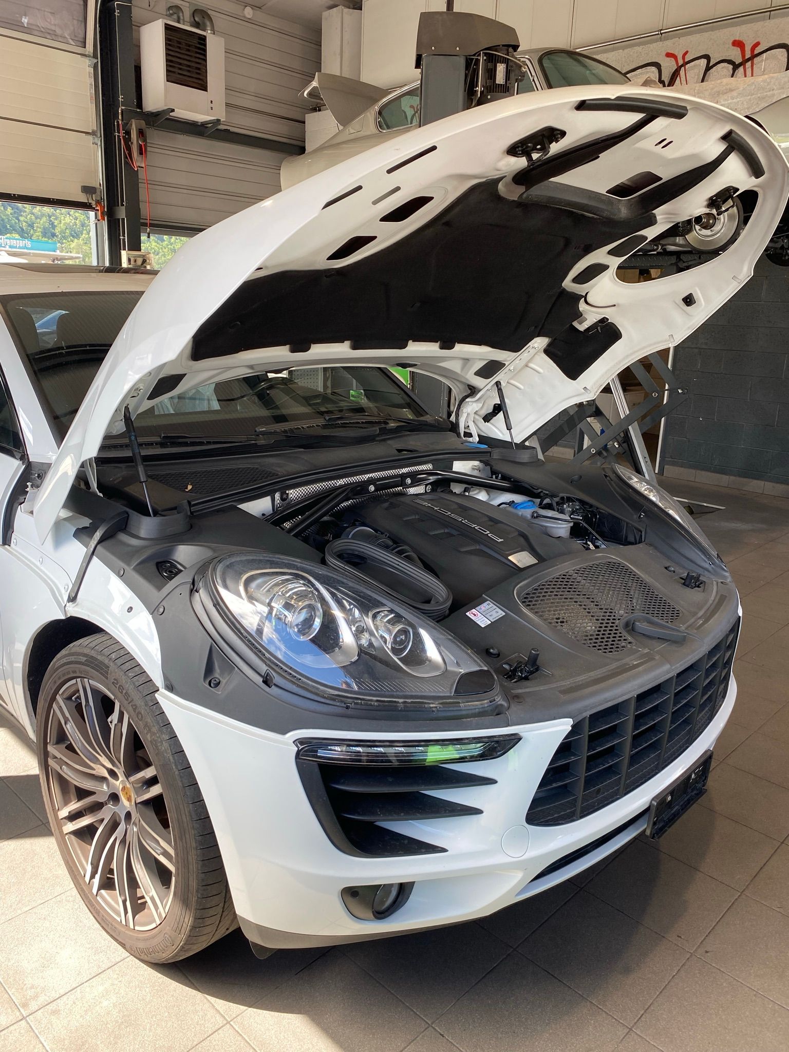 Une porsche macan turbo blanche avec son capot ouvert dans un garage.