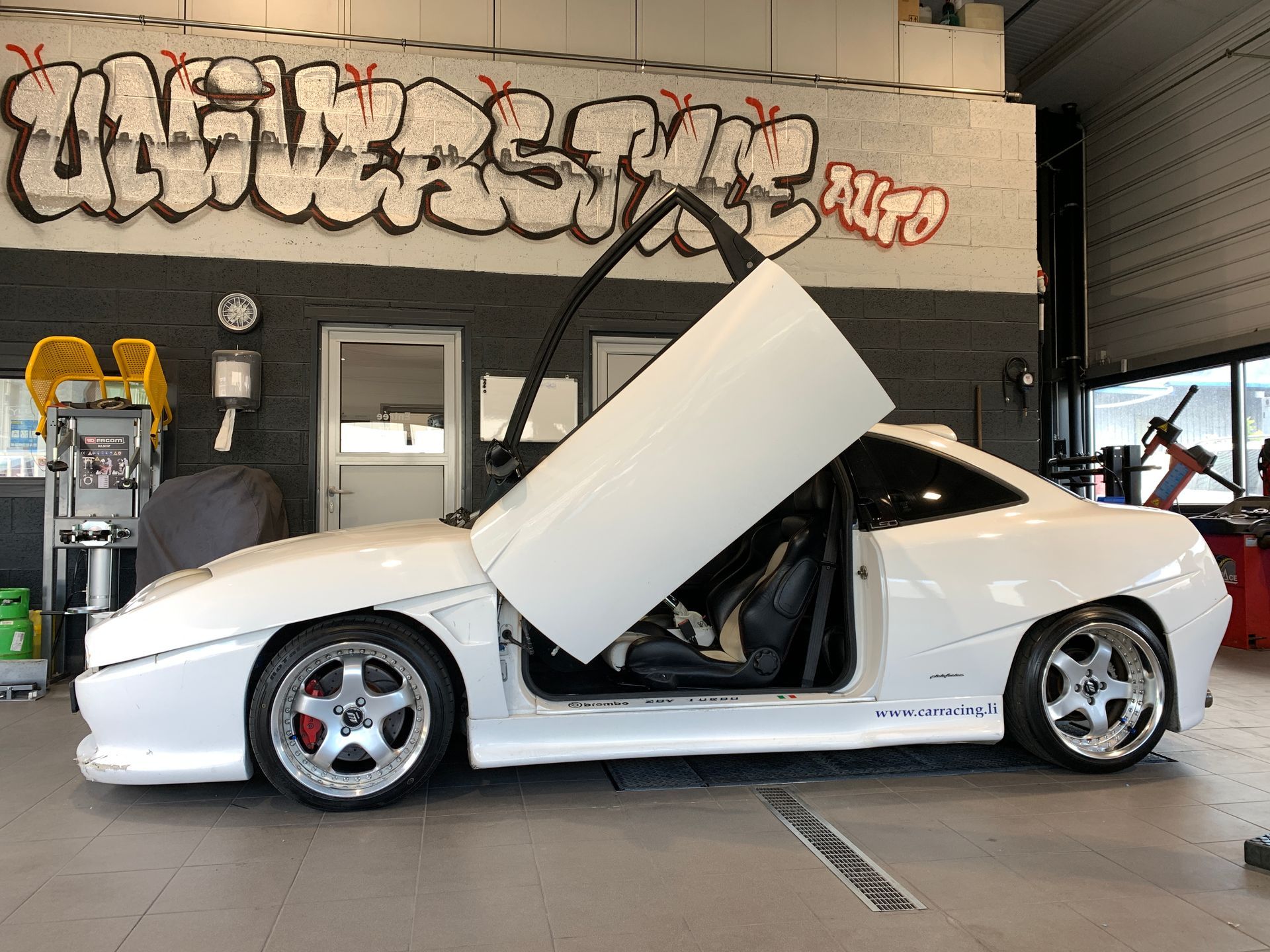 Une voiture de sport blanche est garée dans un garage avec ses portes ouvertes.