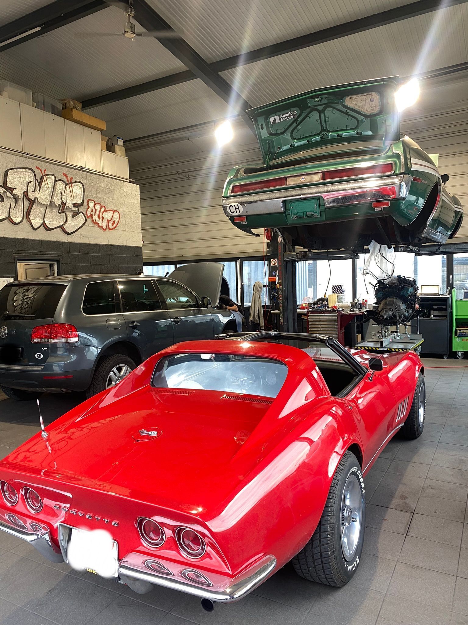 Une corvette rouge est garée dans un garage à côté d'une mustang verte.