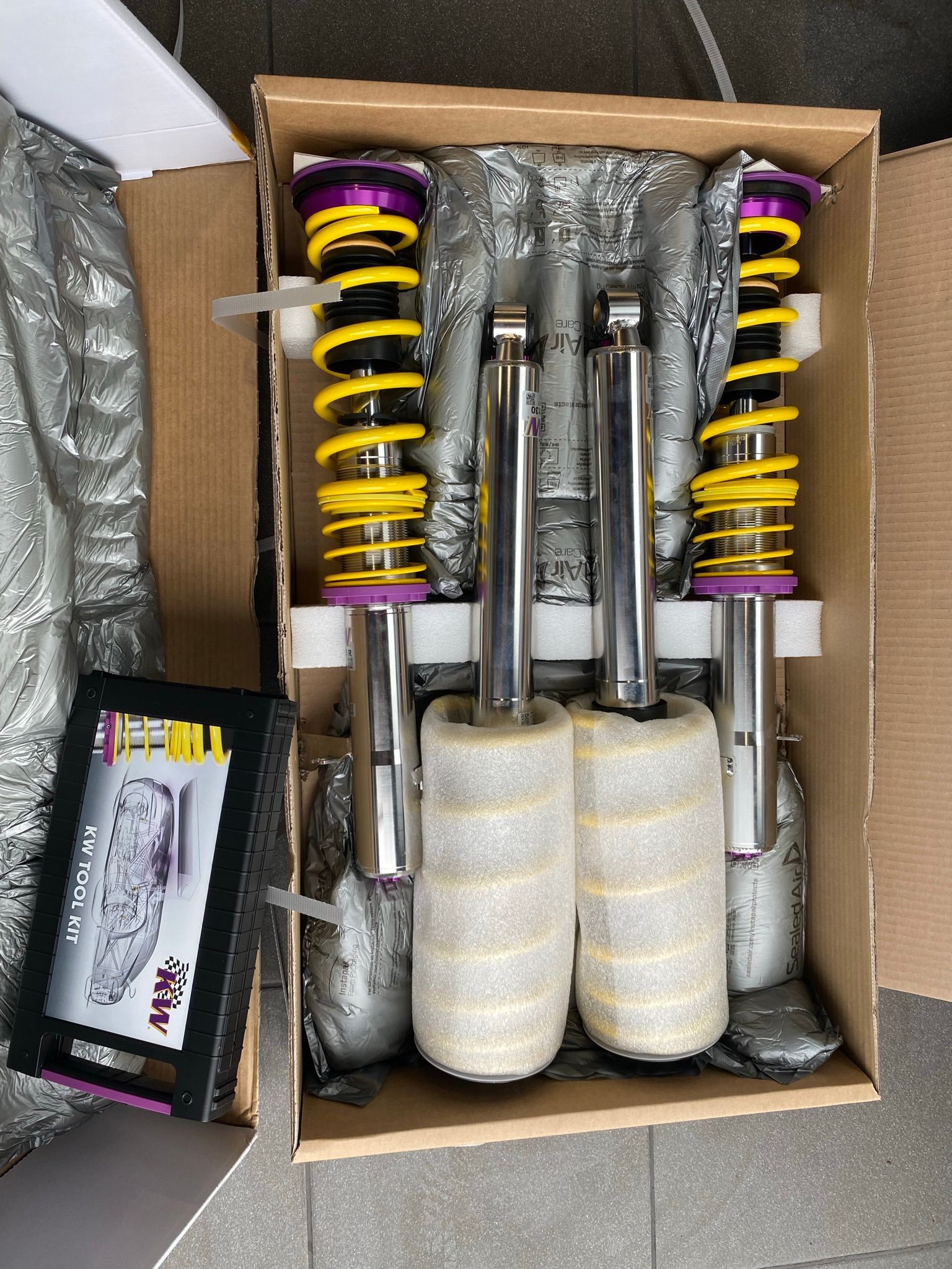 Une boîte d'amortisseurs est posée sur un sol carrelé.