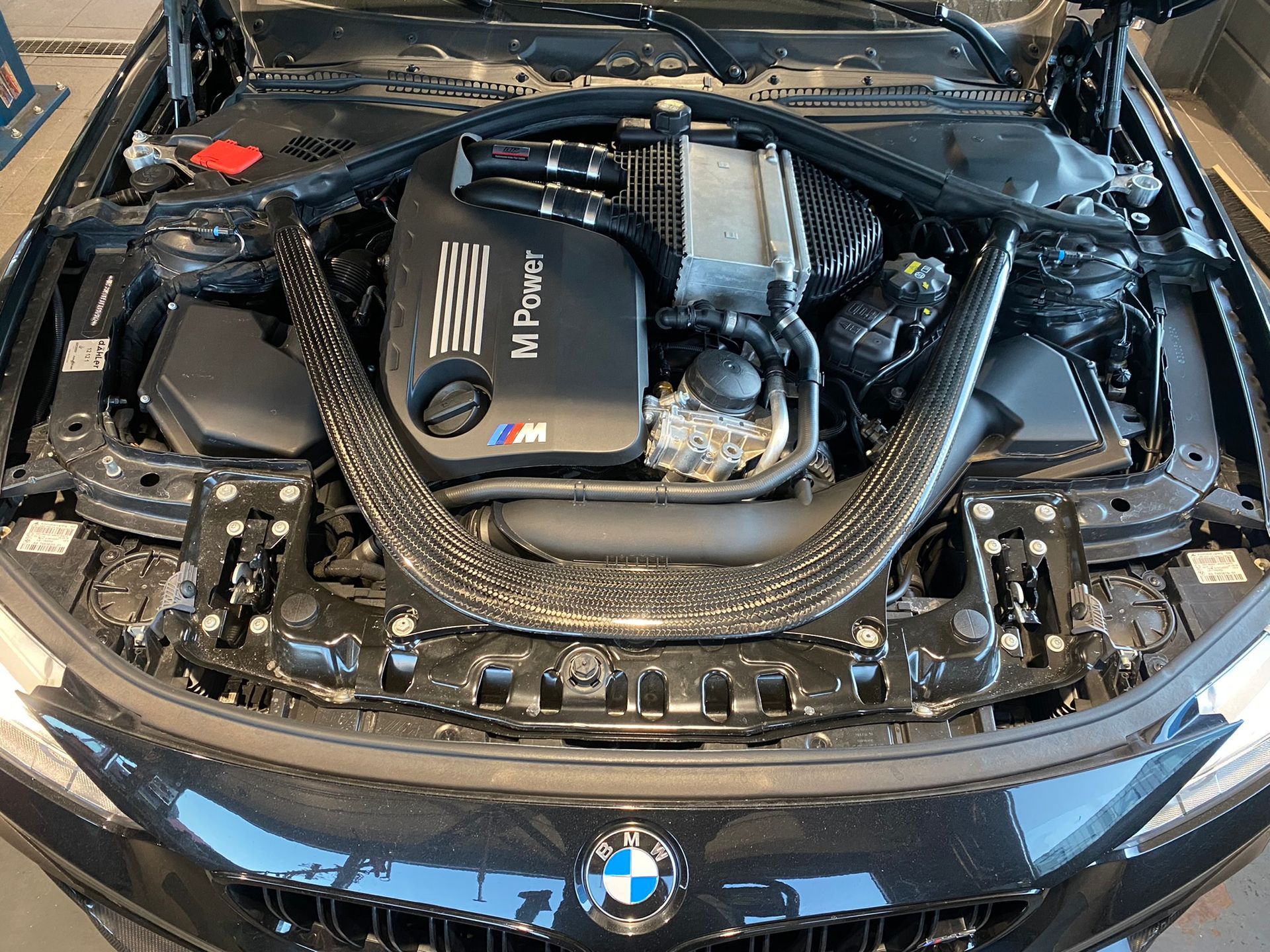 Le moteur d'une bmw m4 noire est visible sous le capot.