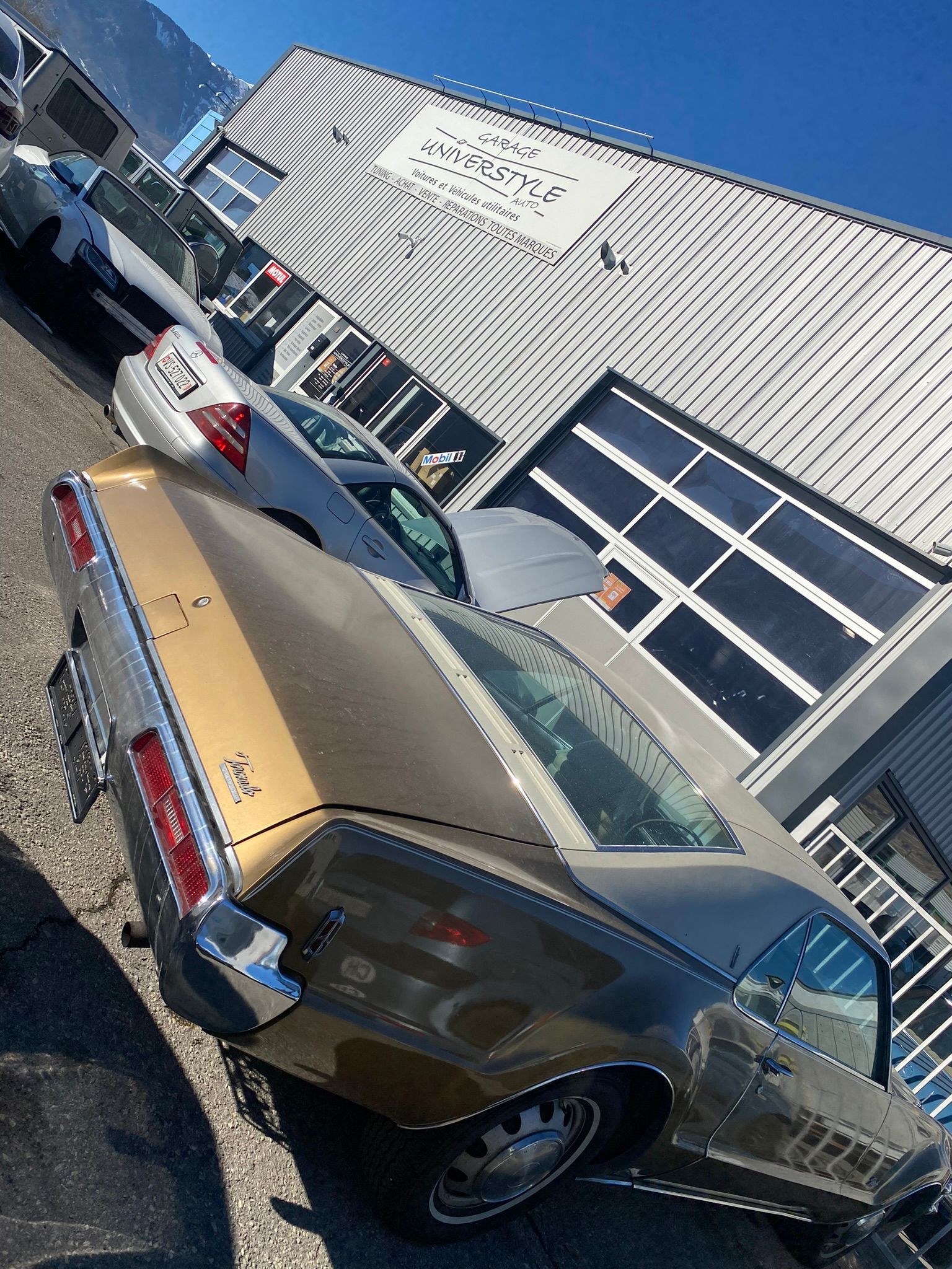 Une voiture argent et or est garée devant un immeuble.