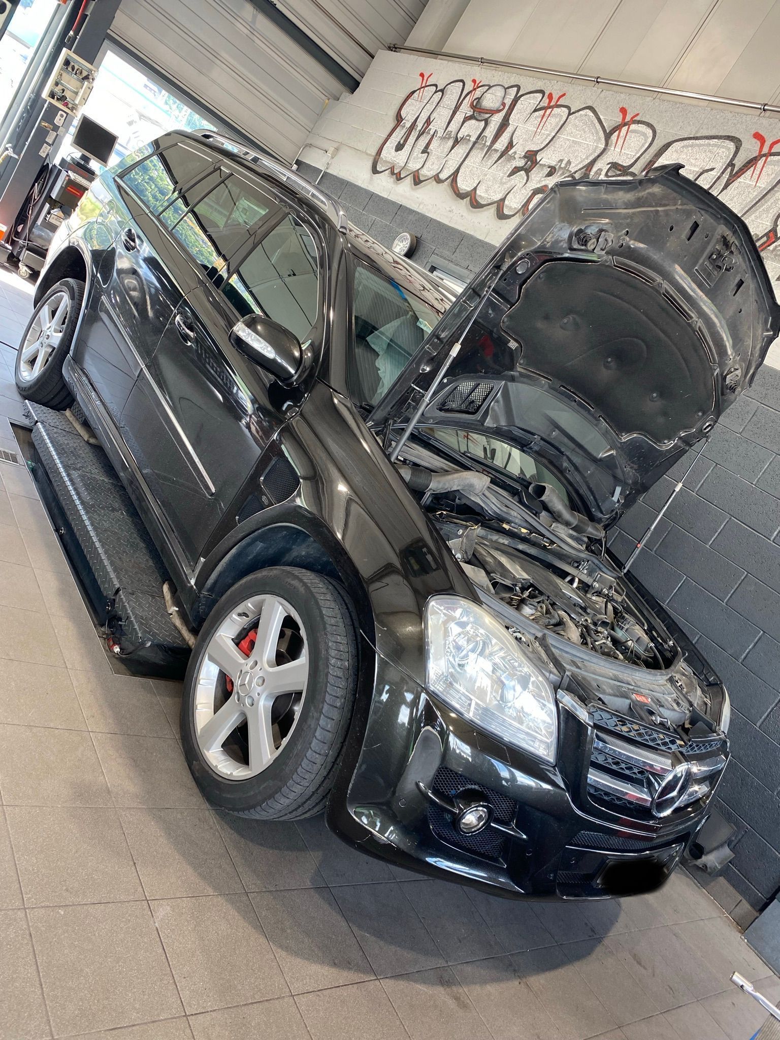Un SUV noir avec le capot relevé est garé dans un garage.