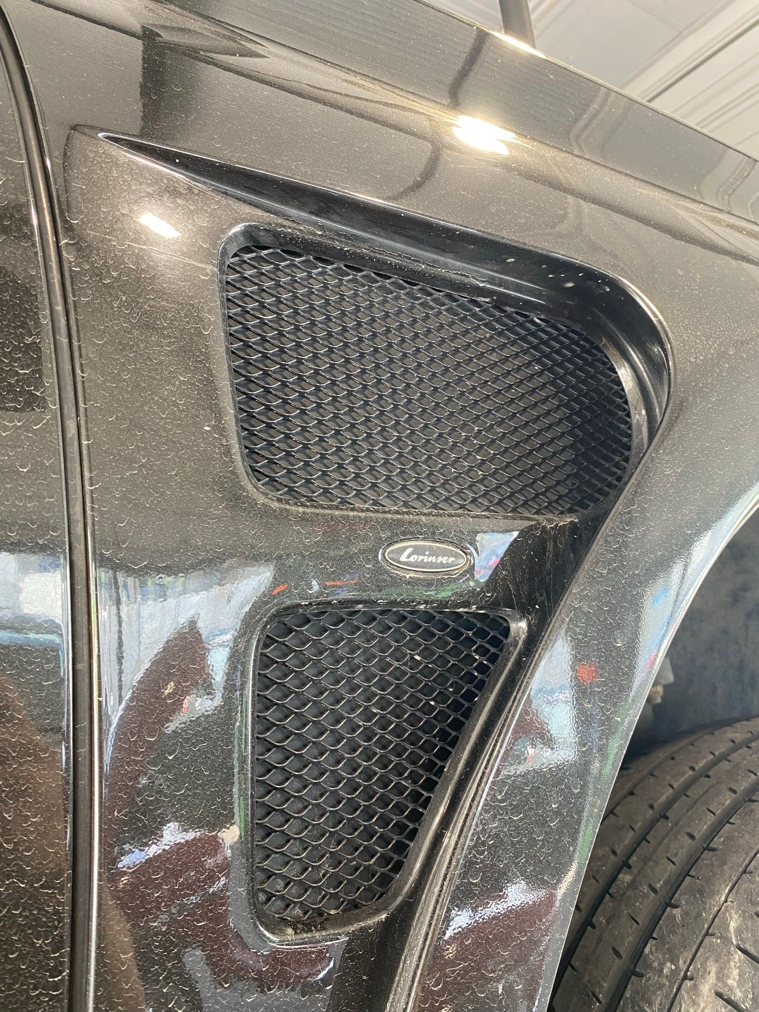 Un gros plan de l'aile d'une voiture noire avec une calandre en maille.