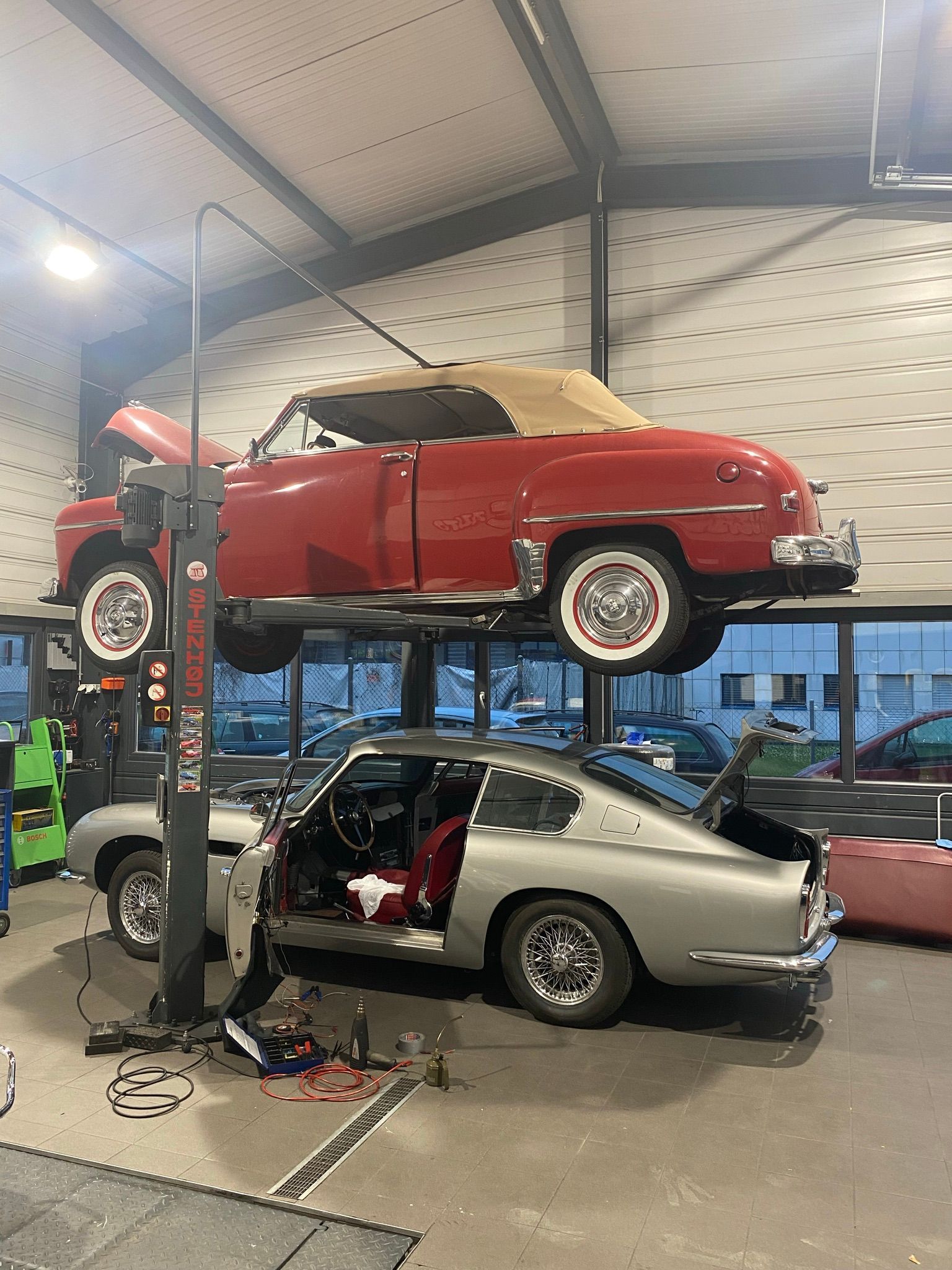 Deux voitures sont posées sur un ascenseur dans un garage.