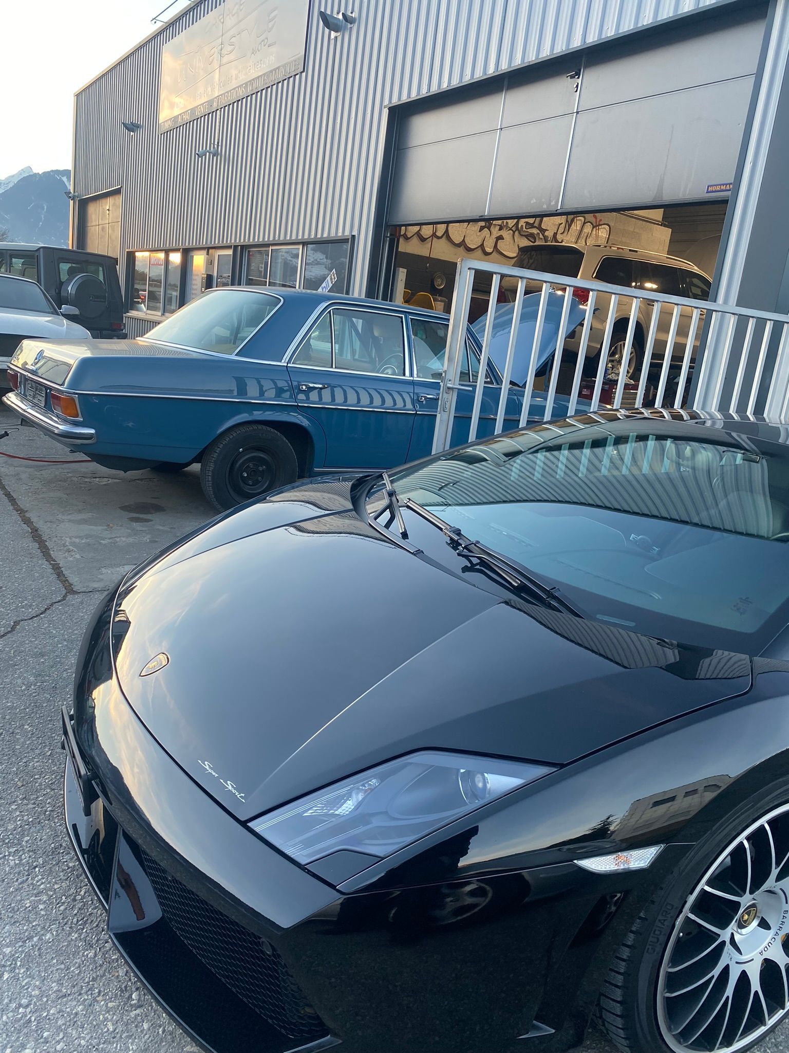 Une voiture noire est garée devant un immeuble à côté d’une voiture bleue.